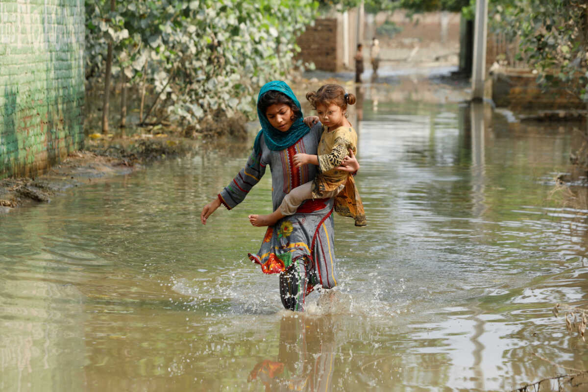 A girl carries her sibling as she walks through stranded flood water, following rains and floods during the monsoon season in Nowshera, Pakistan September 4, 2022. REUTERS