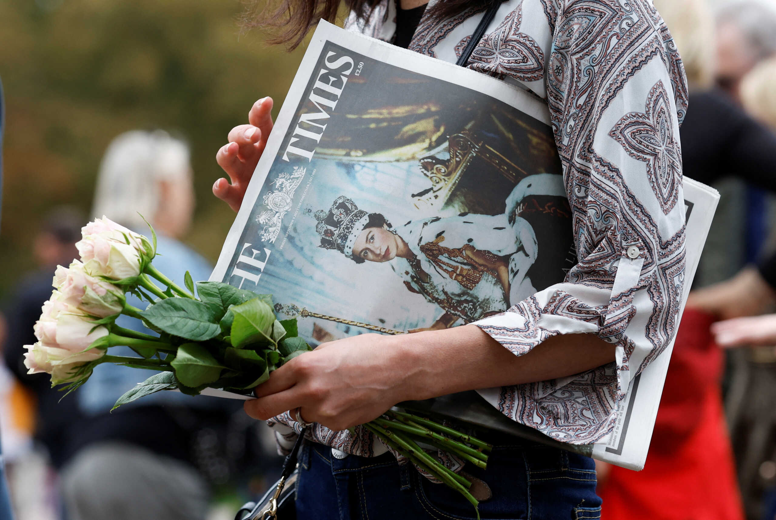 A woman holds flowers and a newspaper depicting Britain's Queen Elizabeth at Windsor Castle, following Queen's passing, in Windsor, Britain, September 9, 2022. REUTERS