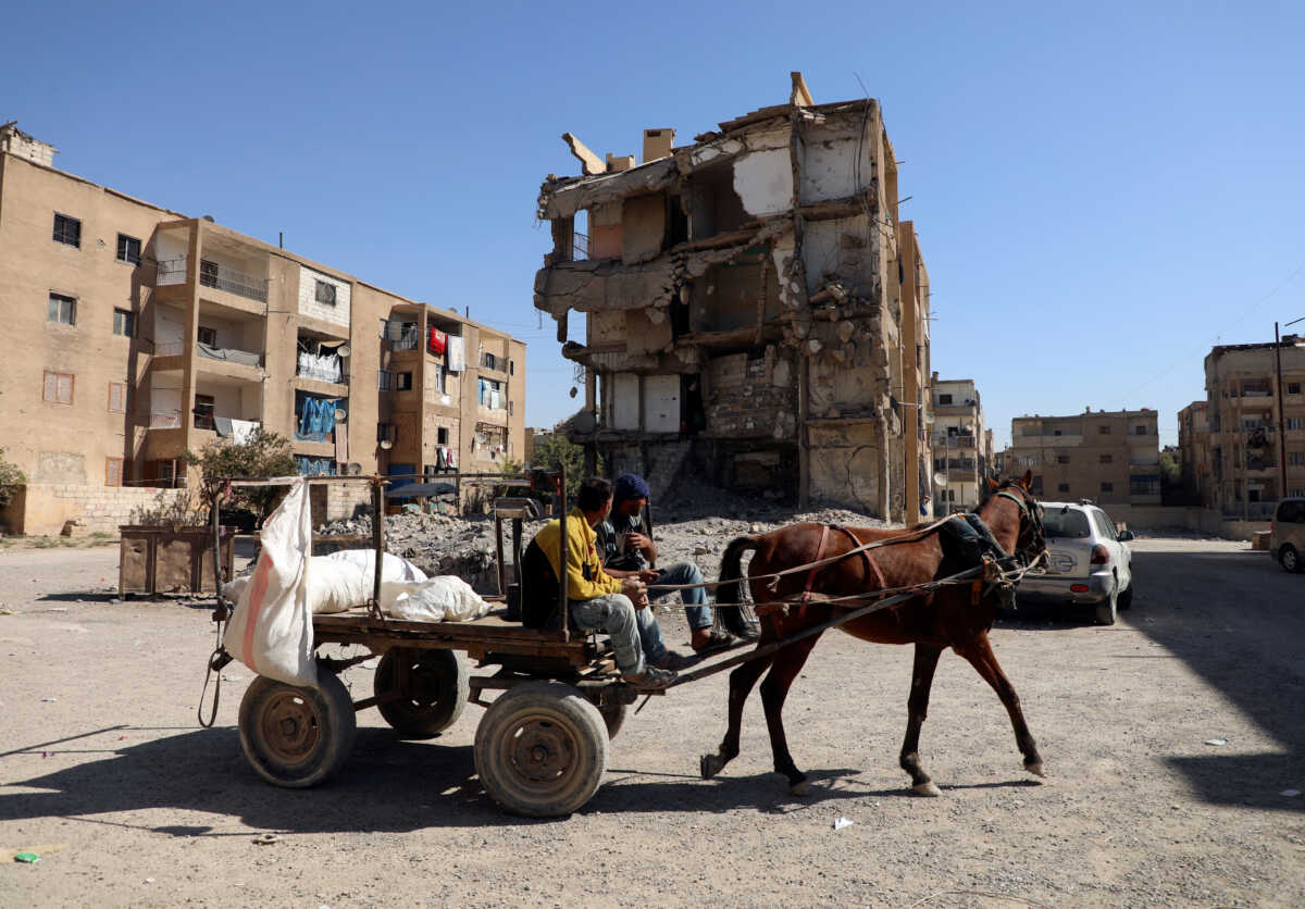 Men ride a horse cart past a damaged a building in Raqqa, Syria October 12, 2022. REUTERS