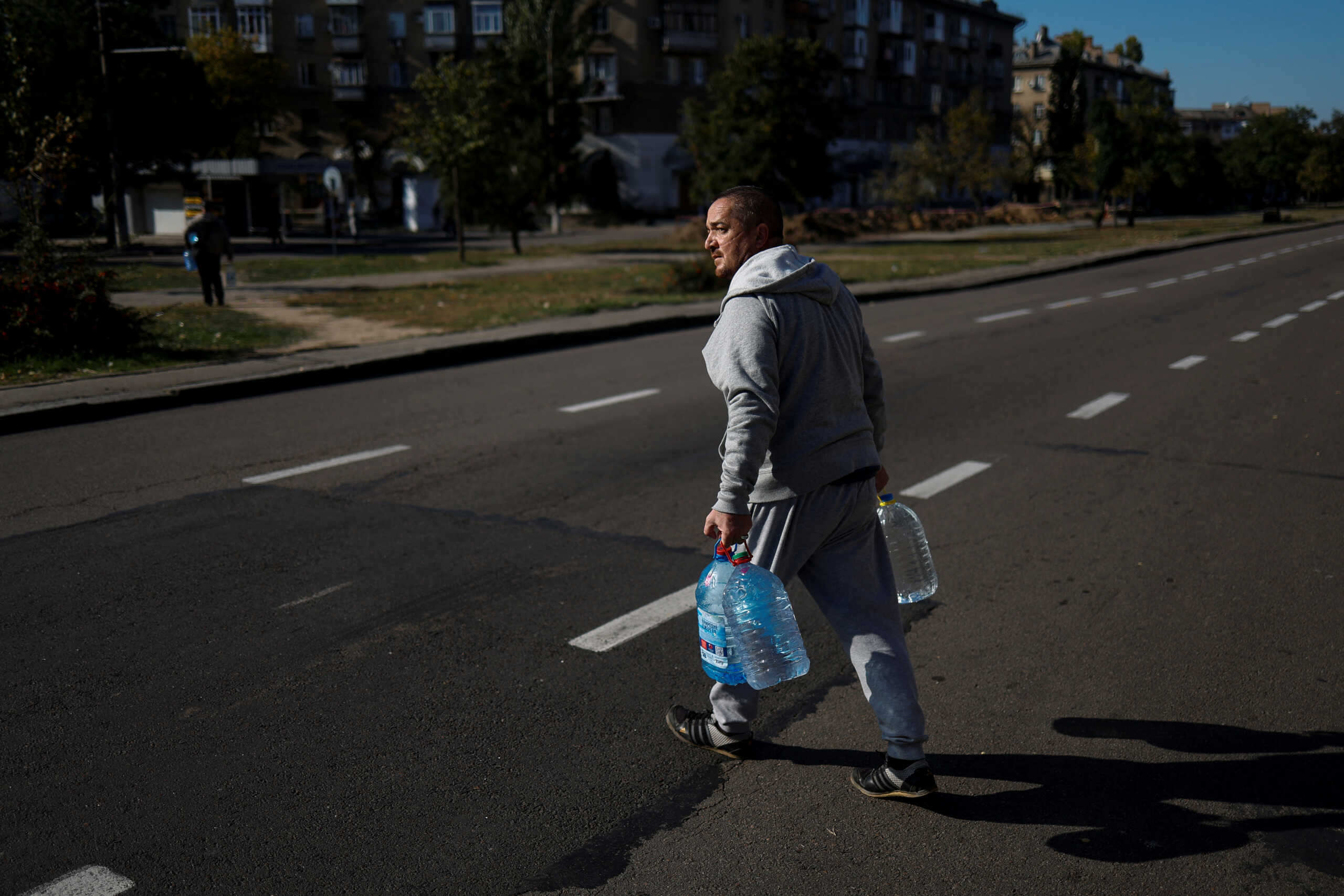 A local man crosses a street with filled bottles of fresh drinking water, as the main supply pipeline for drinking water for the city was damaged in Kherson region at the beginning of Russia's attack on Ukraine, in Mykolaiv, Ukraine October 16, 2022.  REUTERS