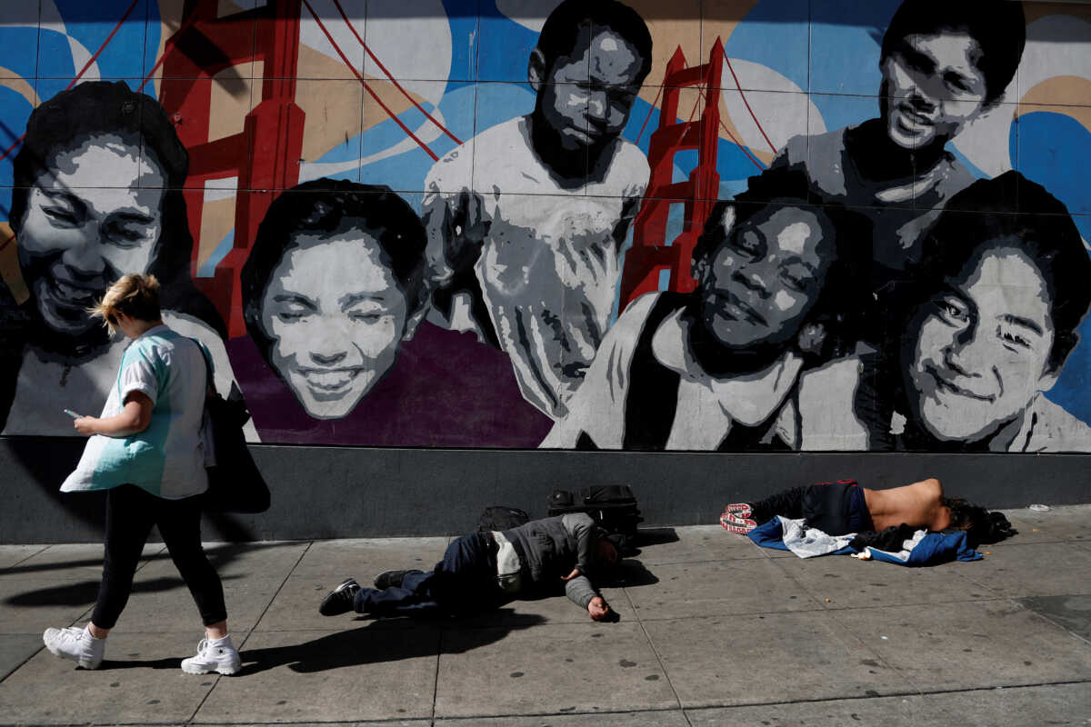 FILE PHOTO: A woman walks past men passed out on the sidewalk n the Tenderloin area of San Francisco, California, U.S., February 28, 2020. Picture taken February 28, 2020. REUTERS