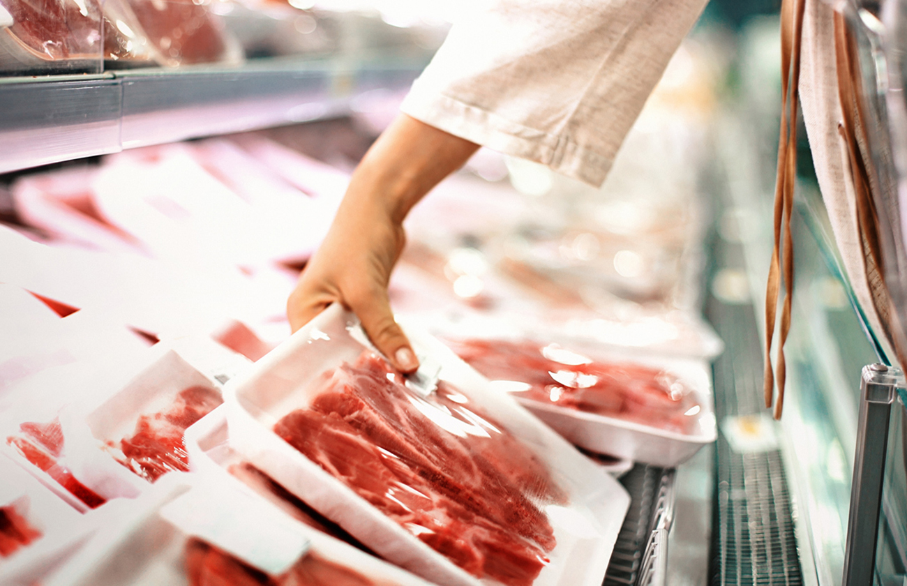 Closeup side view of unrecognizable woman chossing some fresh meat at local supermarket. The meat is cut into chops and packed into one pound packages. She has reached for a package of beef sirloin steaks.