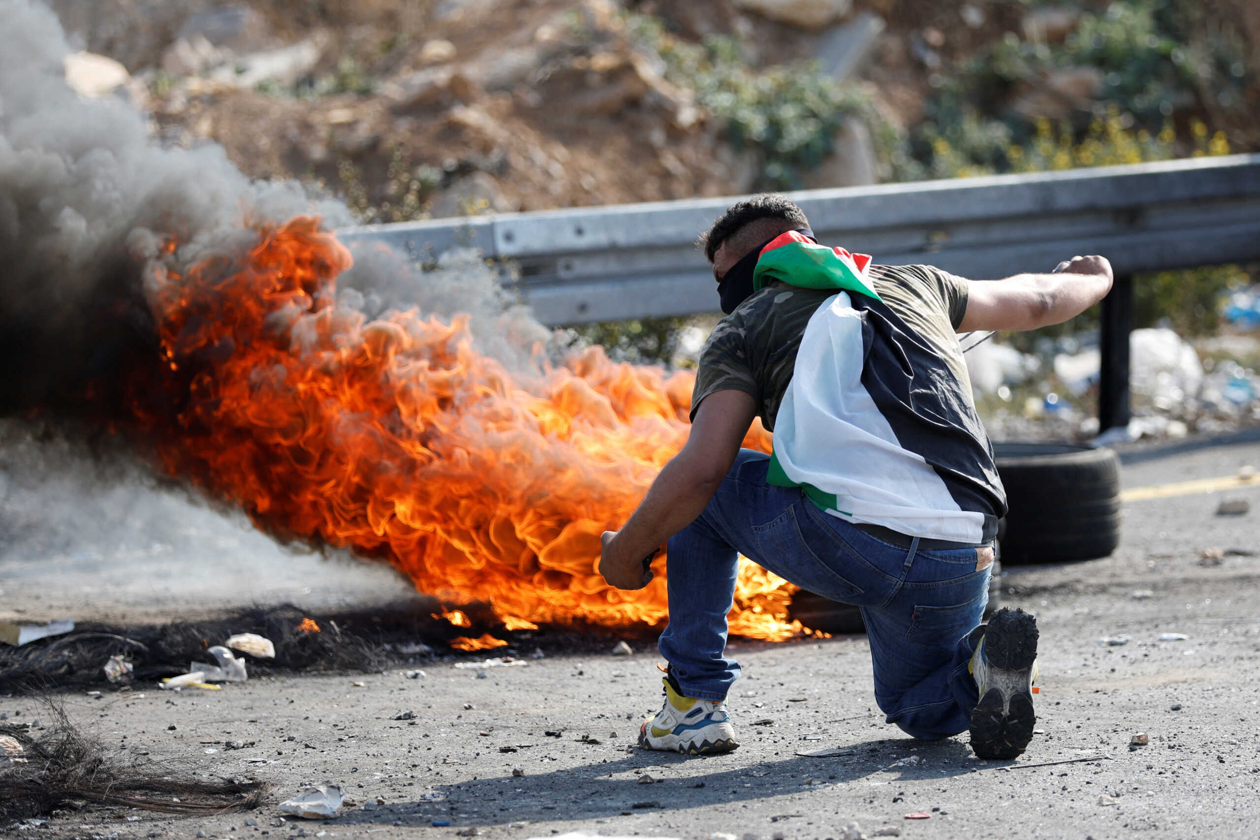 A Palestinian demonstrator throws an object as he stands near a fire, during a protest following the killing of Palestinian assailant Uday Al-Tamimi, near Ramallah in the Israeli-occupied West Bank, October 20, 2022. REUTERS