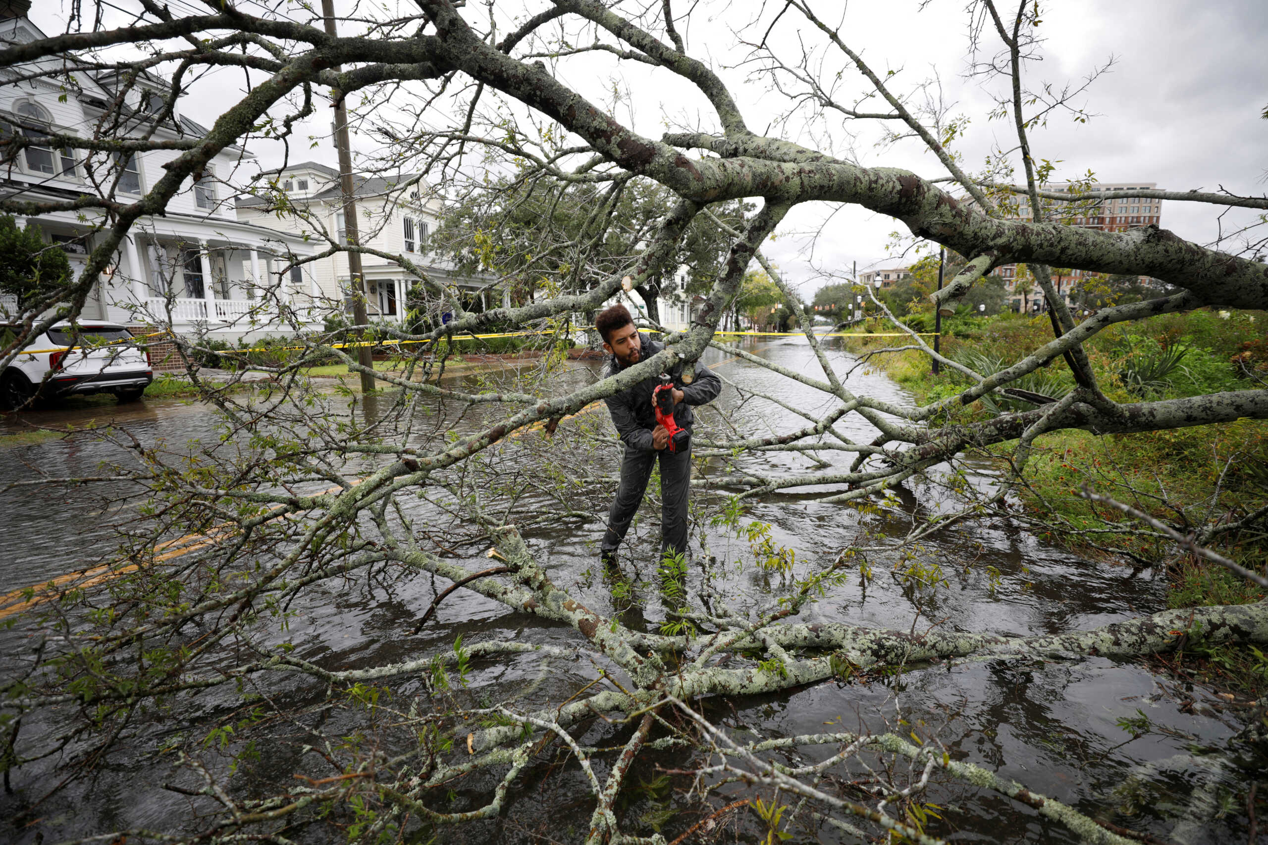 Kieran Holloway, a 25-year-old visiting from Colombia, South Carolina, volunteers to cut away a tree that fell on a flooded road, as hurricane Ian bears down on Charleston, South Carolina, U.S., September 30, 2022.  REUTERS