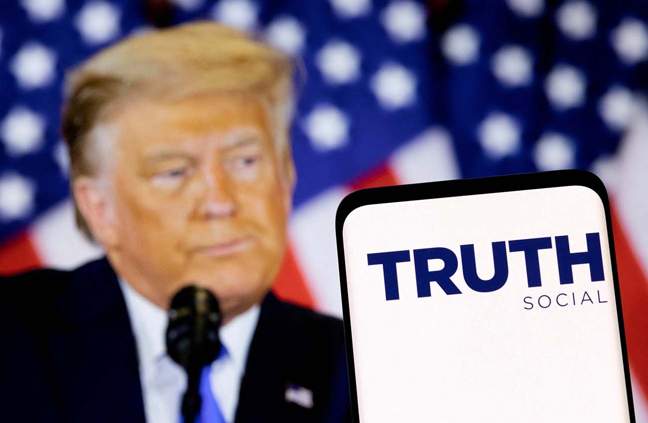 FILE PHOTO: The Truth social network logo is seen on a smartphone in front of a display of former U.S. President Donald Trump in this picture illustration taken February 21, 2022. REUTERS