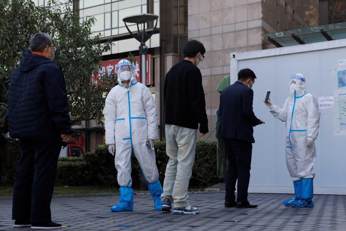 A pandemic prevention worker wears a protective suit as he checks personal details of a man lining up to get a swab test at a testing booth as outbreaks of coronavirus disease (COVID-19) continue in Beijing, China, November 3, 2022. REUTERS