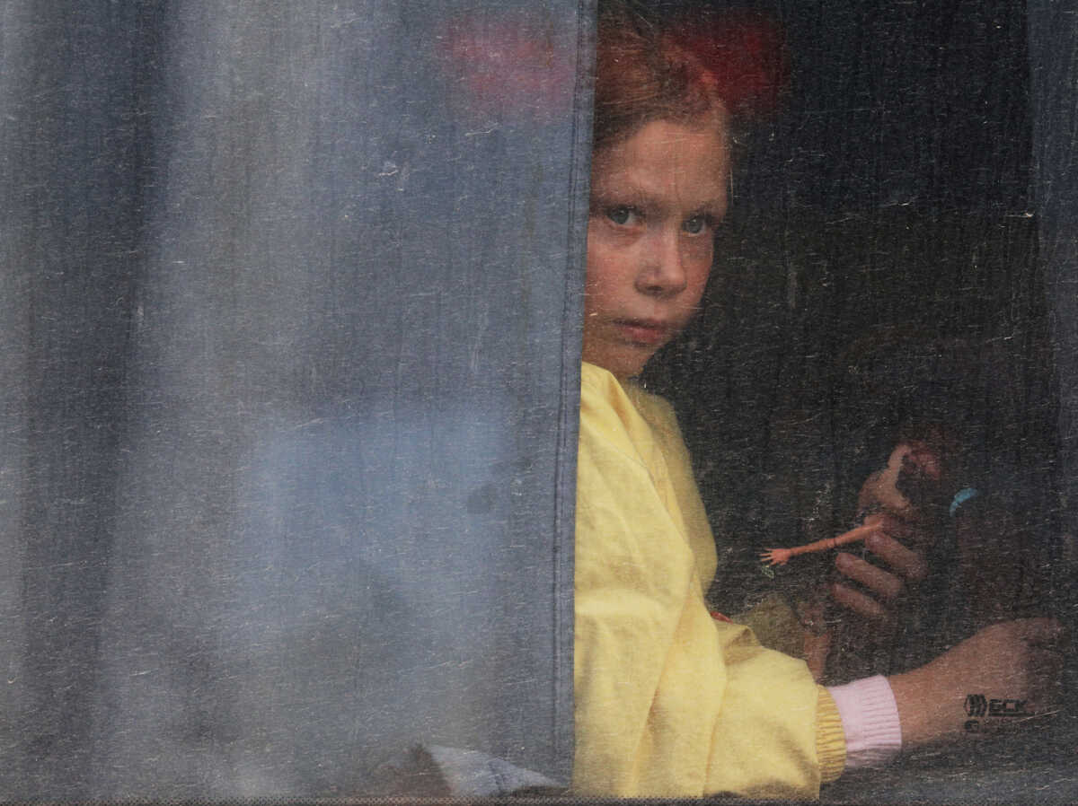A girl looks out of a bus window as civilians evacuated from the Russian-controlled Kherson region of Ukraine arrive at a local railway station, after Russian-installed officials extended an evacuation order to the area along the eastern bank of the Dnipro River, in the town of Dzhankoi, Crimea November 2, 2022. REUTERS