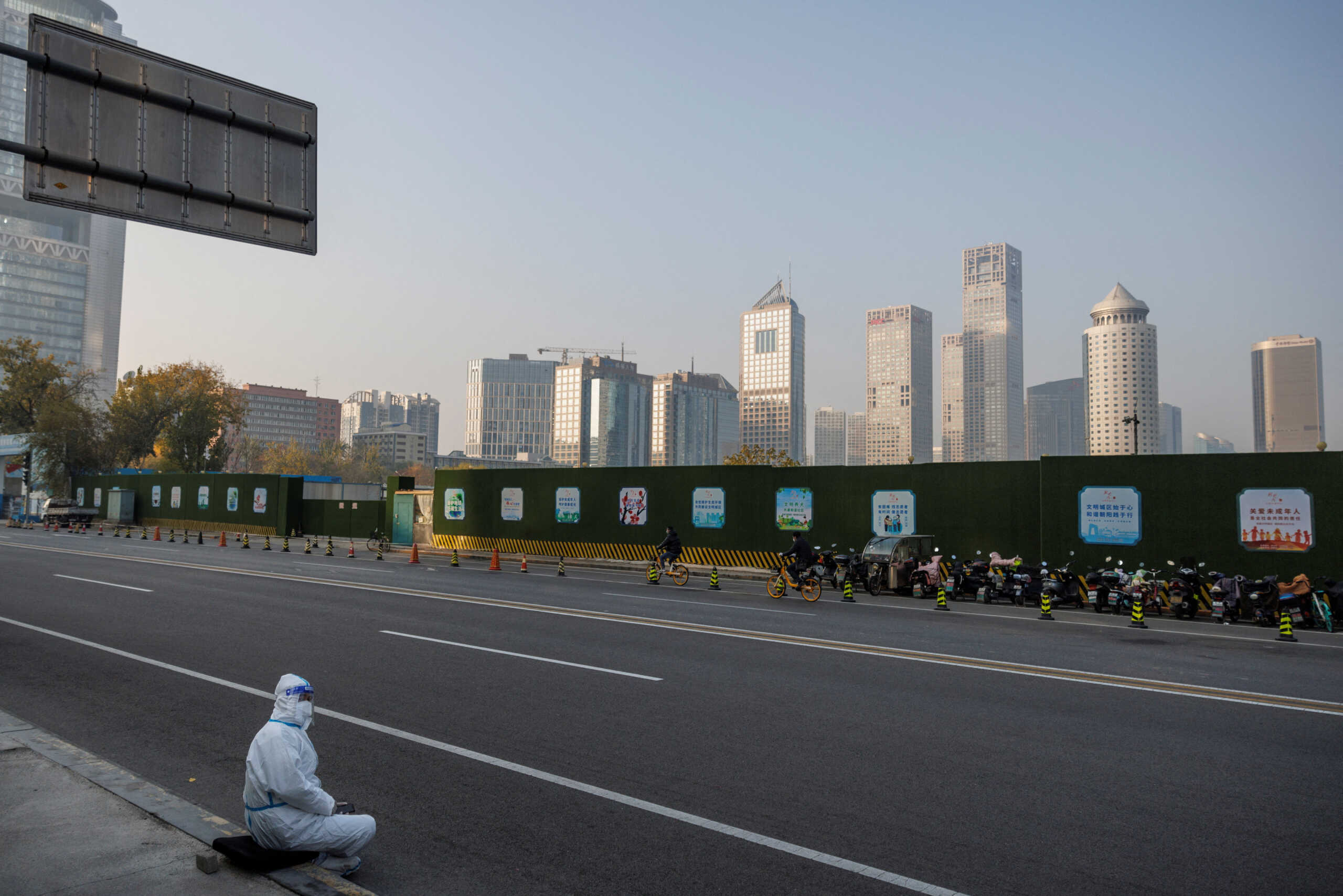An epidemic prevention worker in a protective suit sits on the pavement in the Central Business District (CBD) as outbreaks of the coronavirus disease (COVID-19) continue in Beijing, November 23, 2022. REUTERS