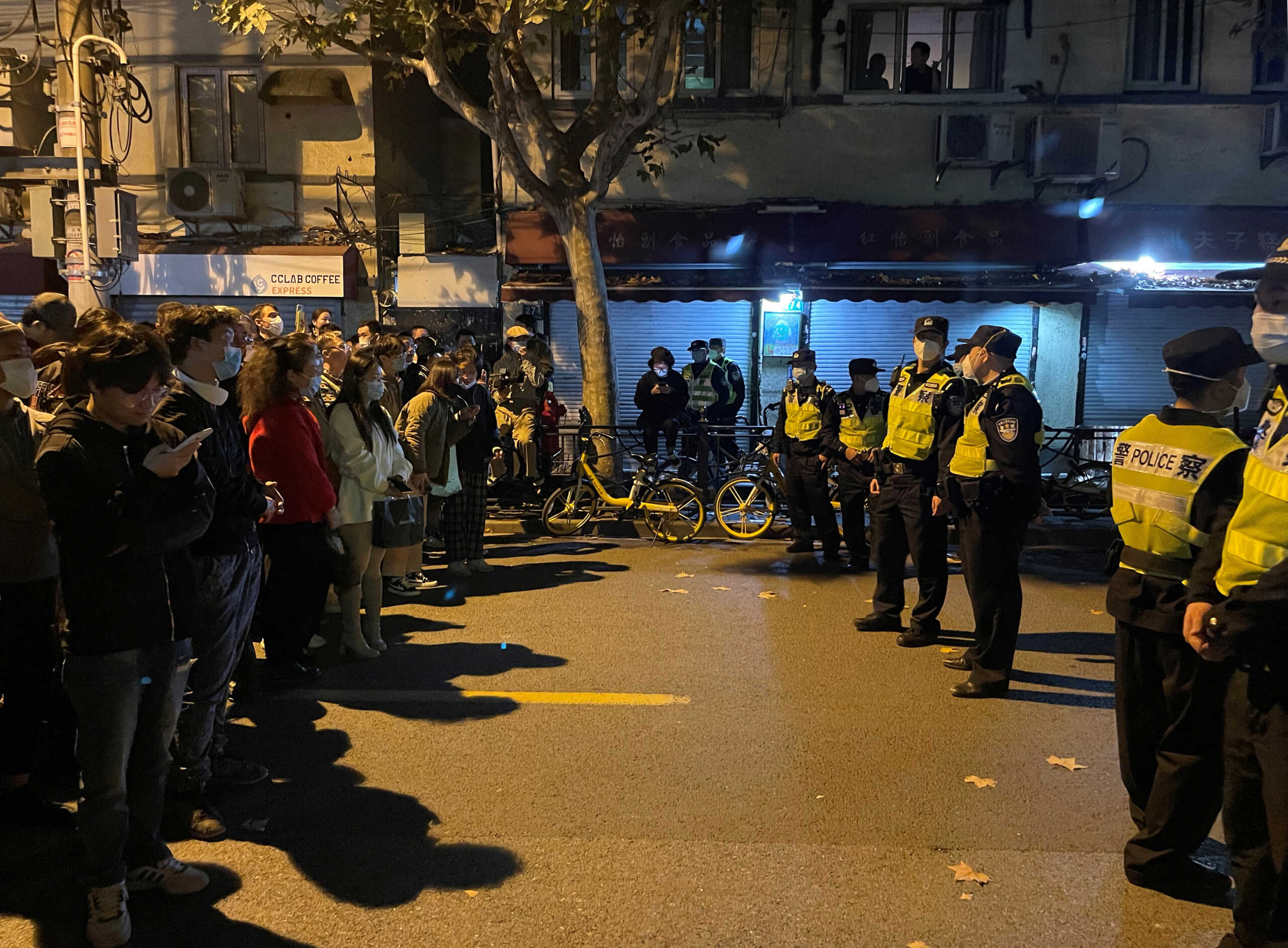 People stand in front of a line of police officers during a demonstration against COVID-19 curbs following the deadly Urumqi fire, in Shanghai, China November 27, 2022. REUTERS