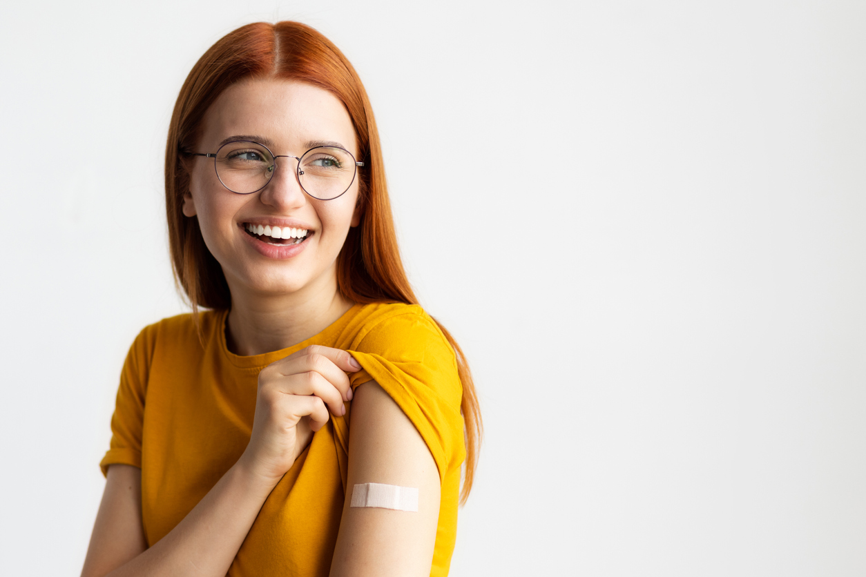 Covid-19 vaccinated caucasian smiling young woman showing arm with plaster
