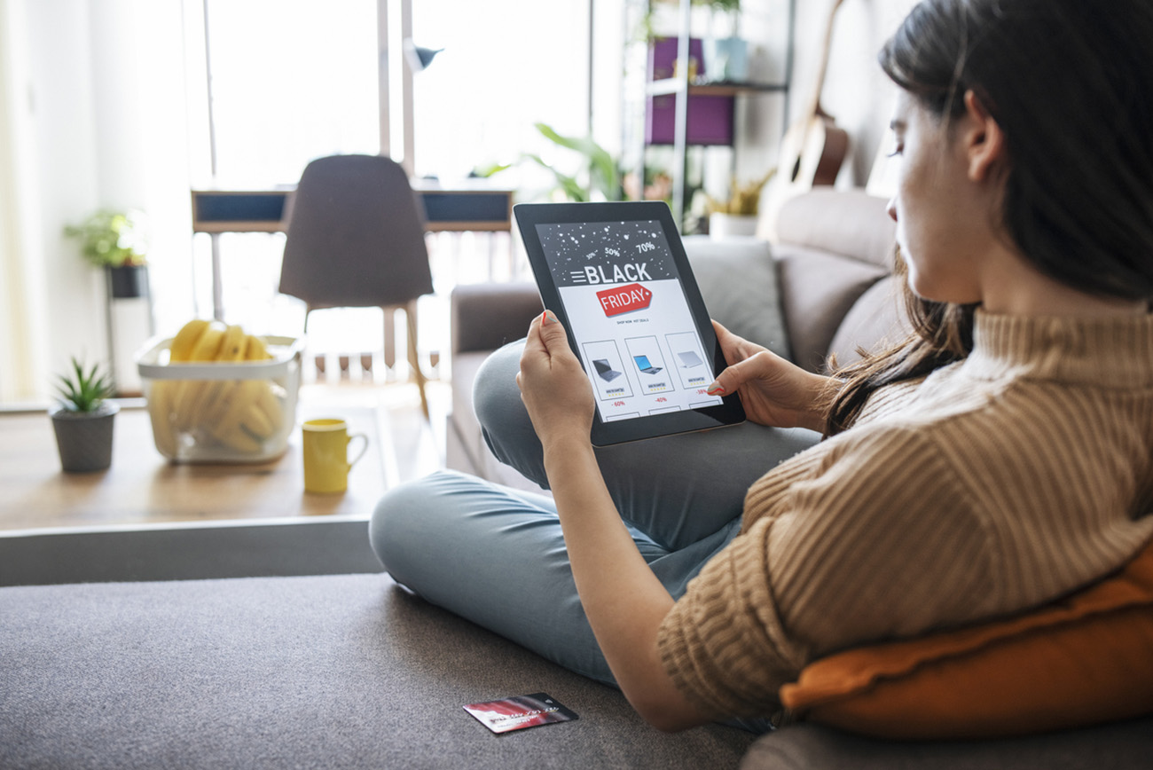 Woman is laying on sofa at home and looking for best discount during Black Friday.