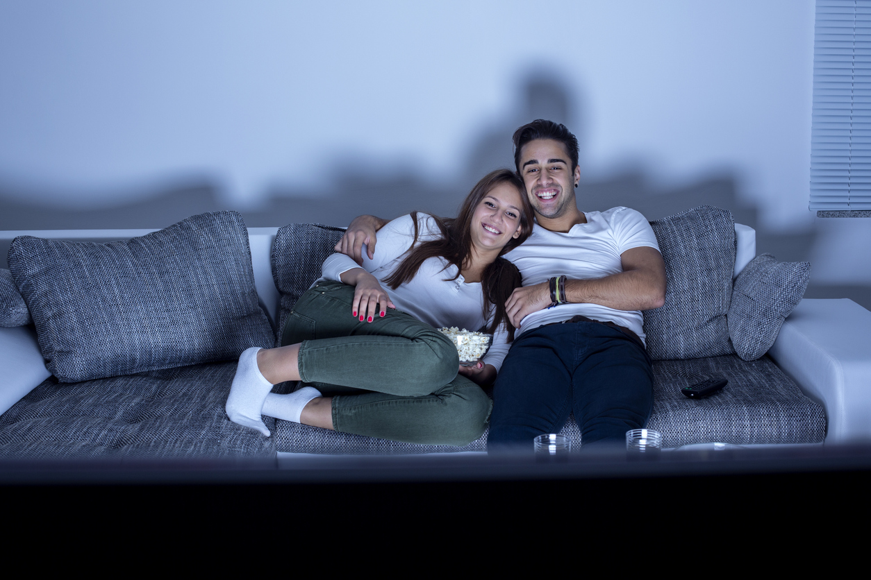Young smiling couple watching a movie at home. Both Caucasian, casual, about 20 years old.