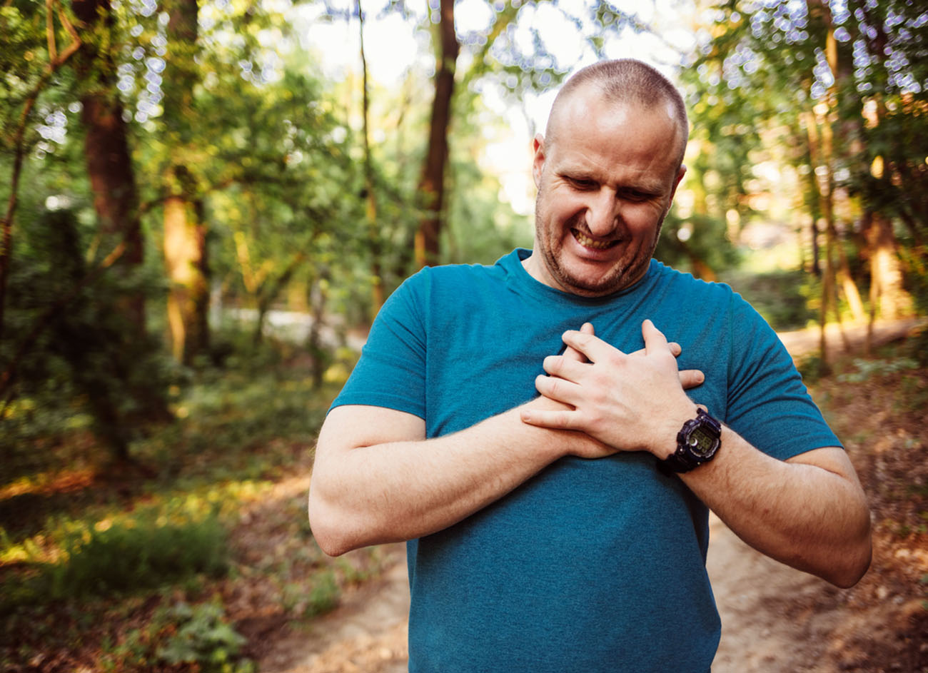 Sport man having heart attack or chest pain after running workout at park. Young man suffering from heart attack while jogging, holding his chest. Sport and Health care concept.