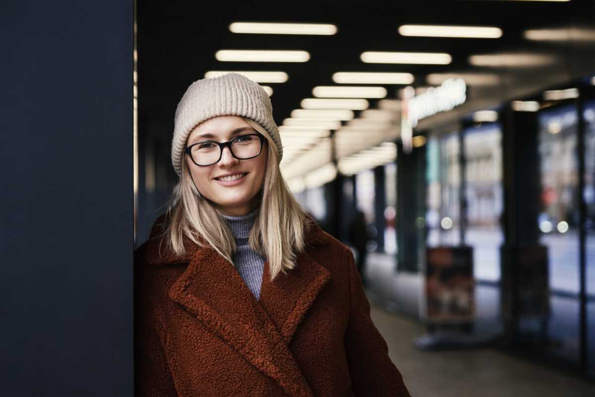 Portrait of beautiful smiling woman in eyeglasses. Woman wearing coat at city. Street walking