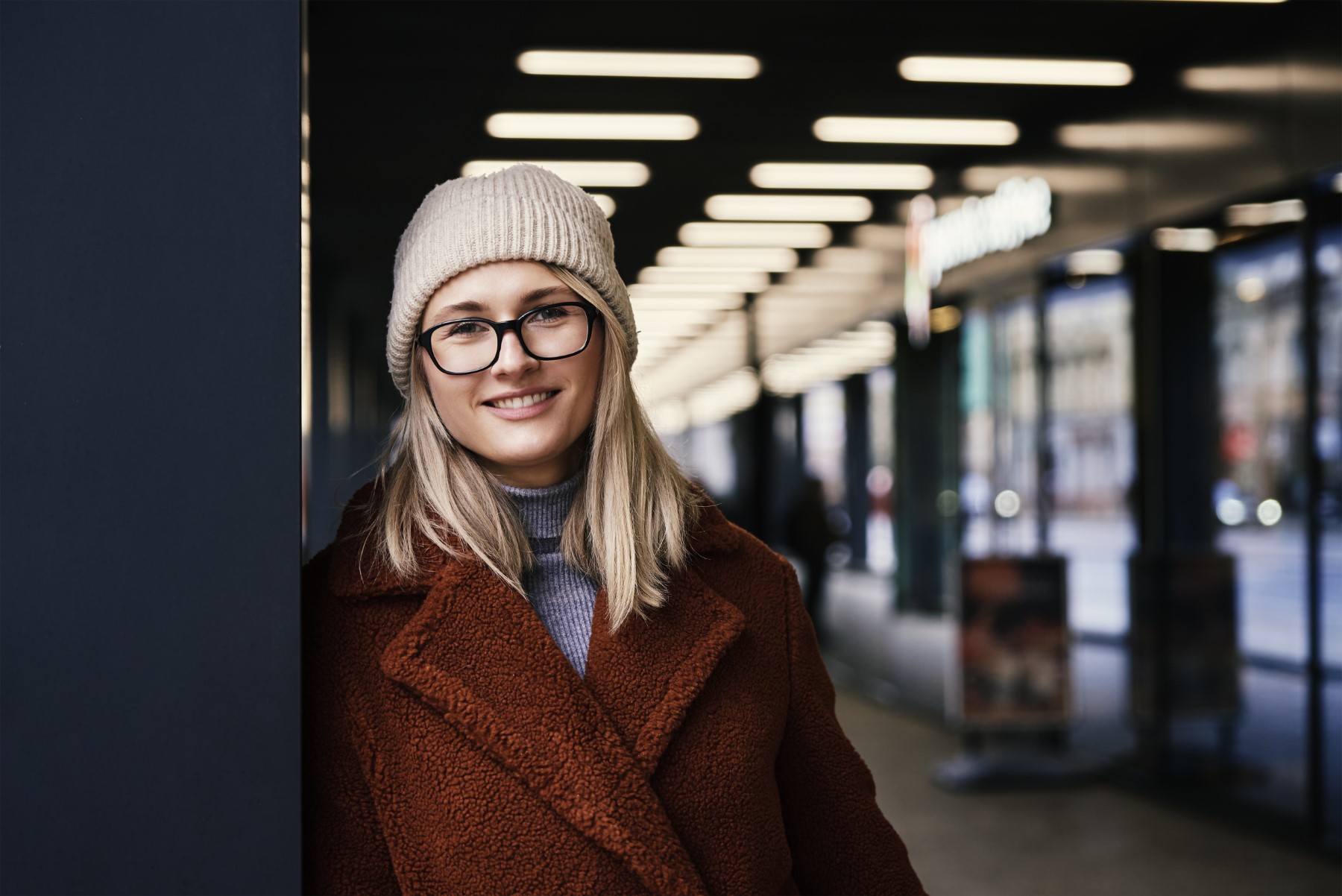 Portrait of beautiful smiling woman in eyeglasses. Woman wearing coat at city. Street walking