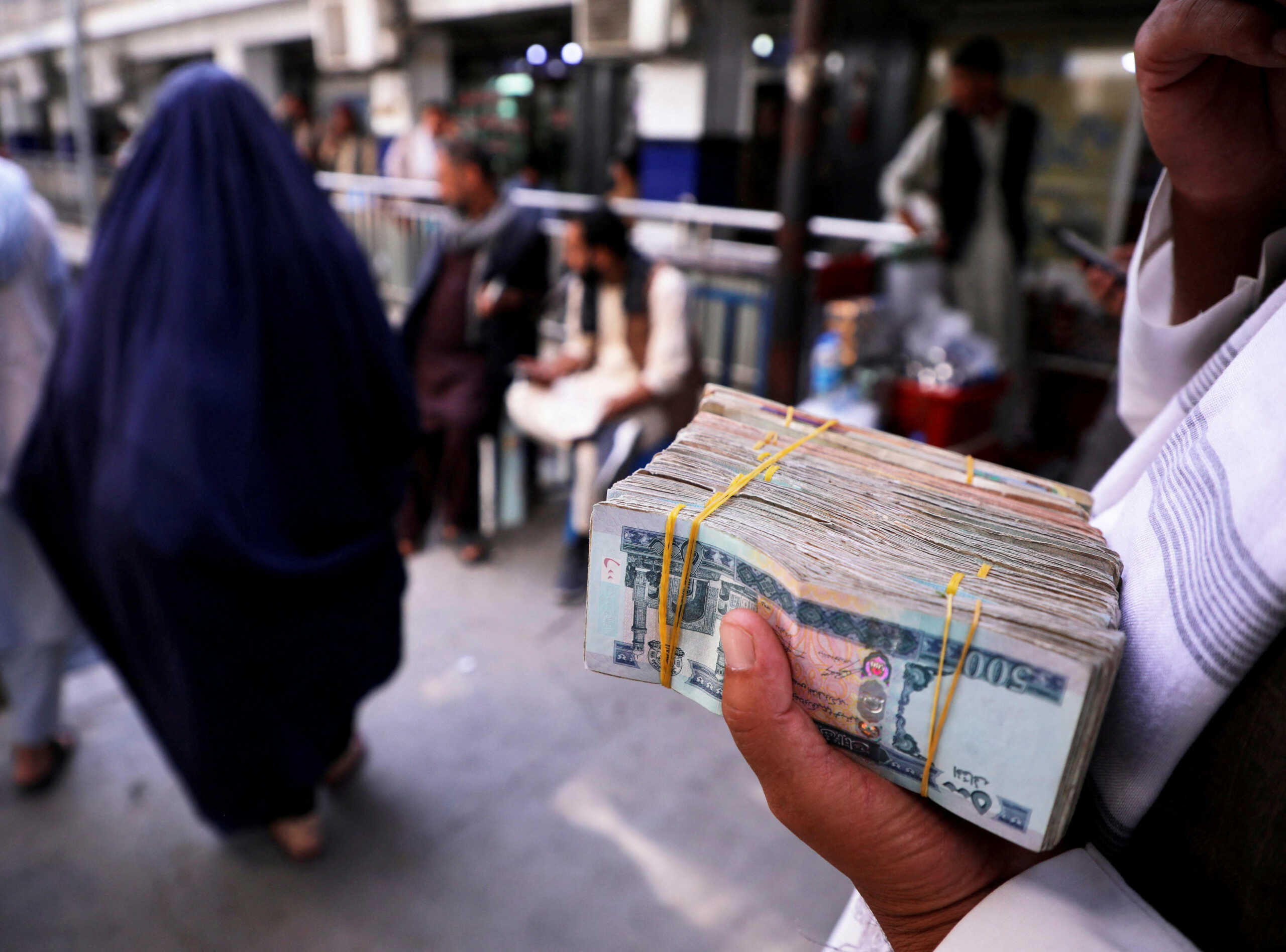 FILE PHOTO: A person holds a bundle of Afghan afghani banknotes at a money exchange market after banks and markets reopened following the Taliban takeover in Kabul, Afghanistan, September 4, 2021. REUTERS