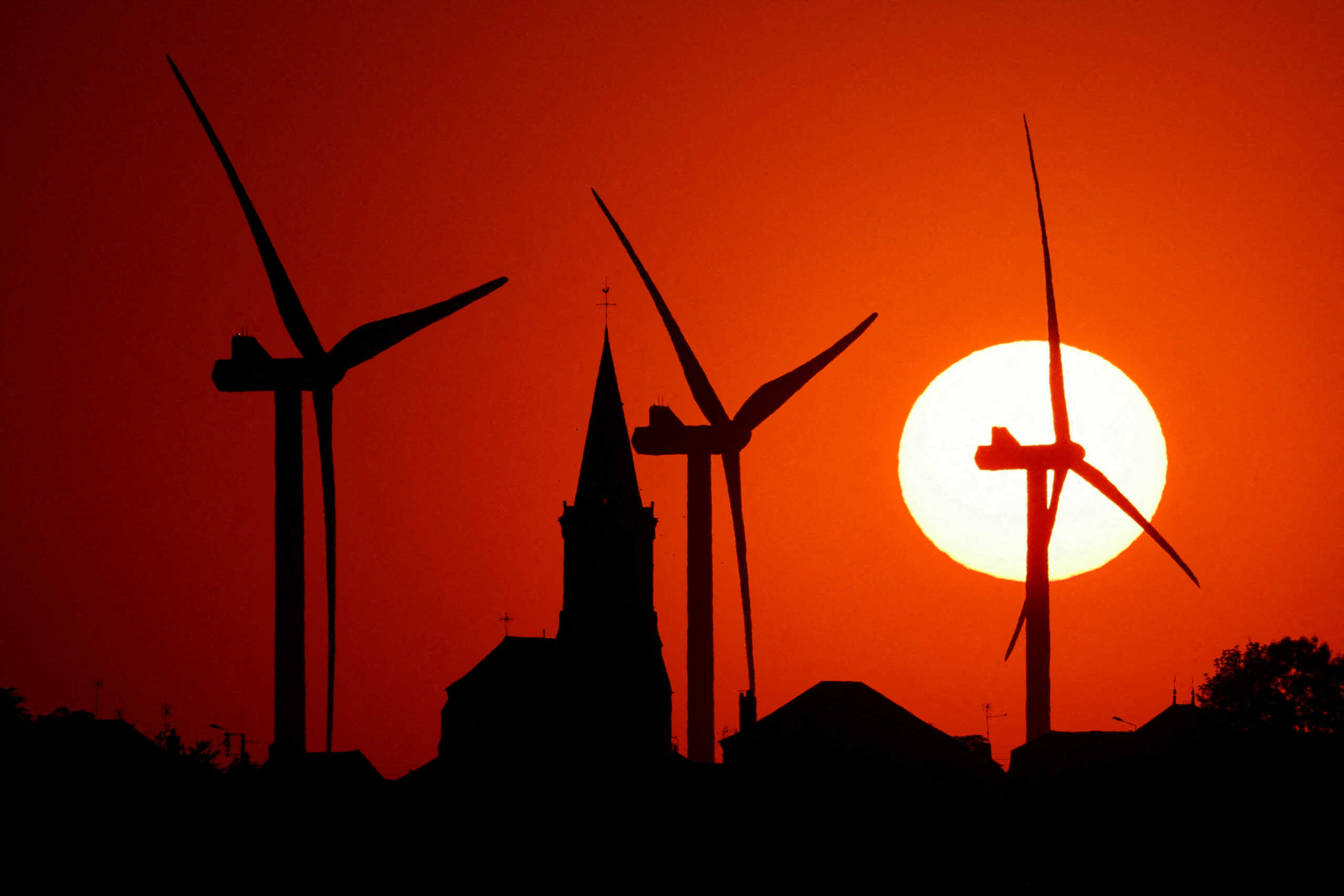 FILE PHOTO: Power-generating windmill turbines and the church of the village are pictured during sunset at a wind park in Bethencourt, France August 11, 2022. REUTERS