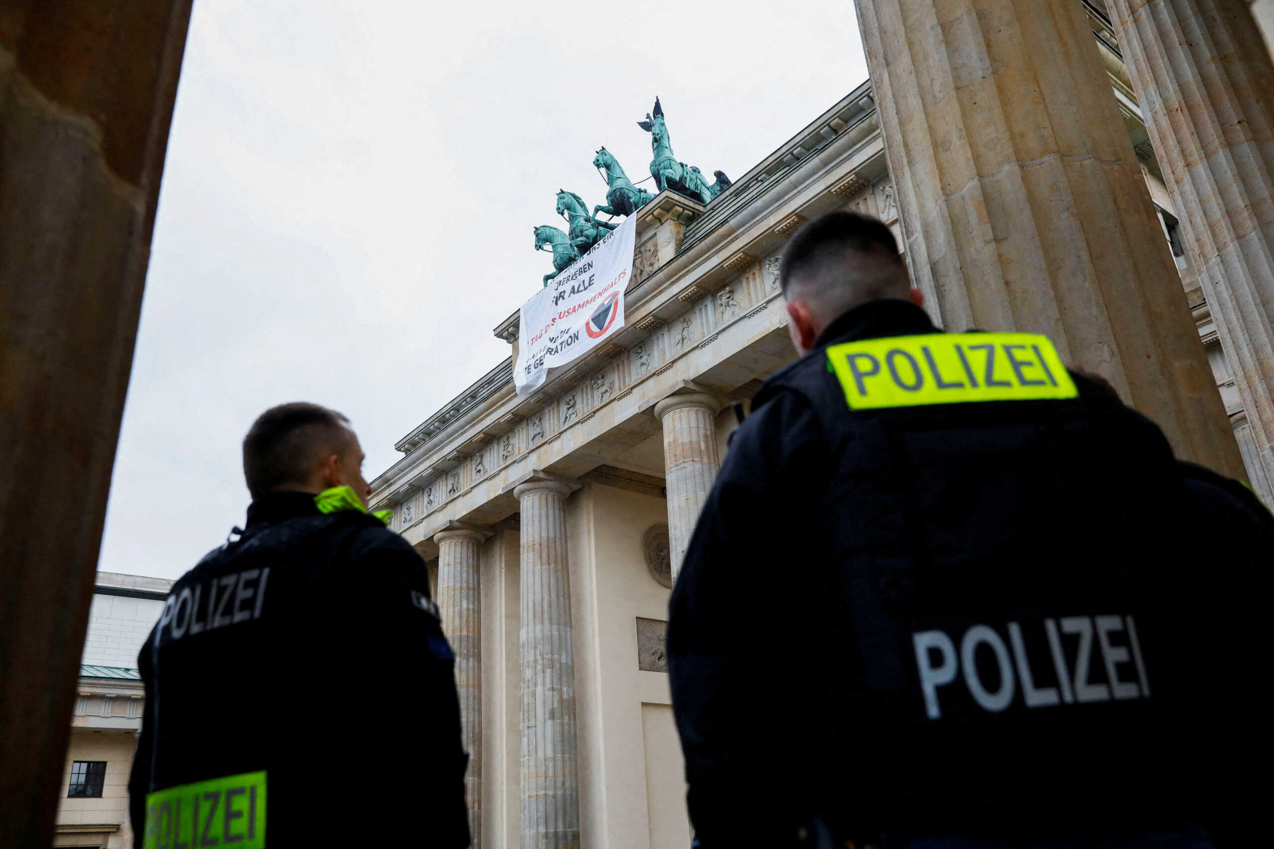 Police officers watch as climate activists of the "Last Generation" drop a billboard reading 'we wish a survival for everyone' from the Brandenburg Gate in Berlin, Germany November 9, 2022. REUTERS