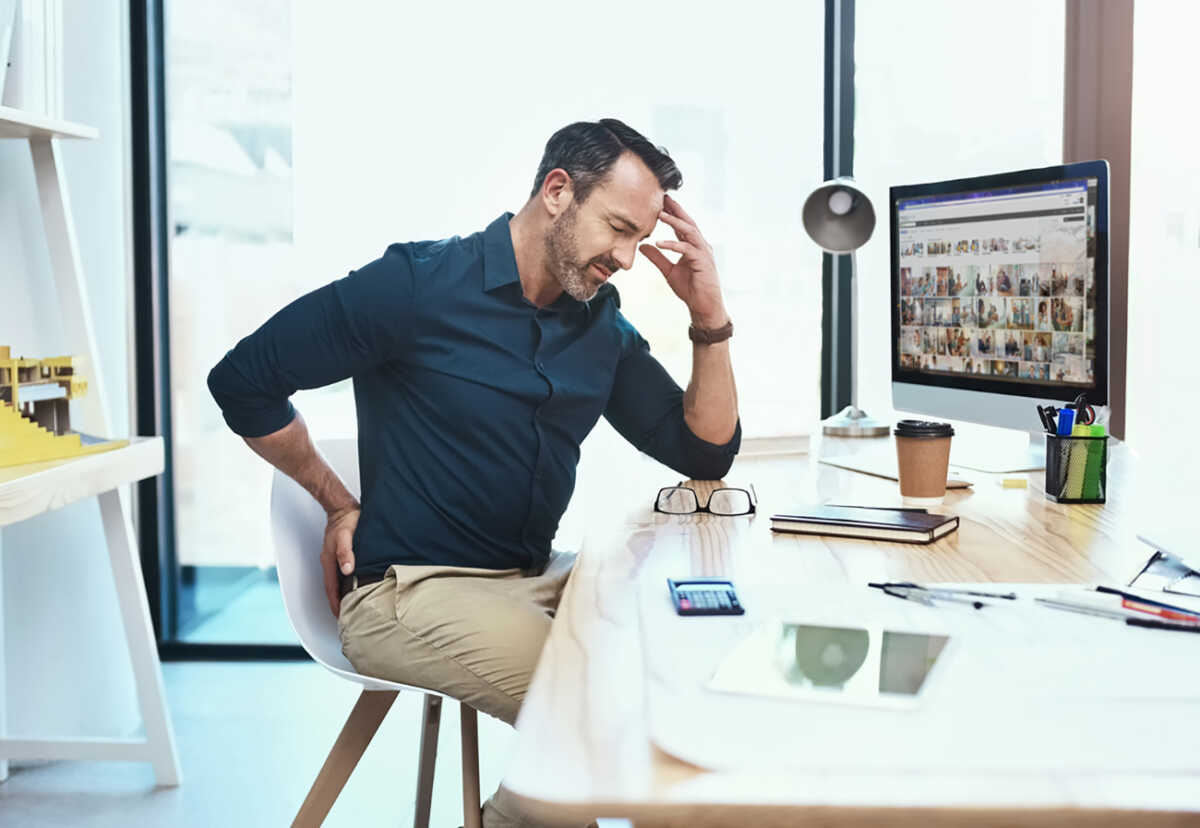 Shot of a mature businessman experiencing back pain while working at his desk