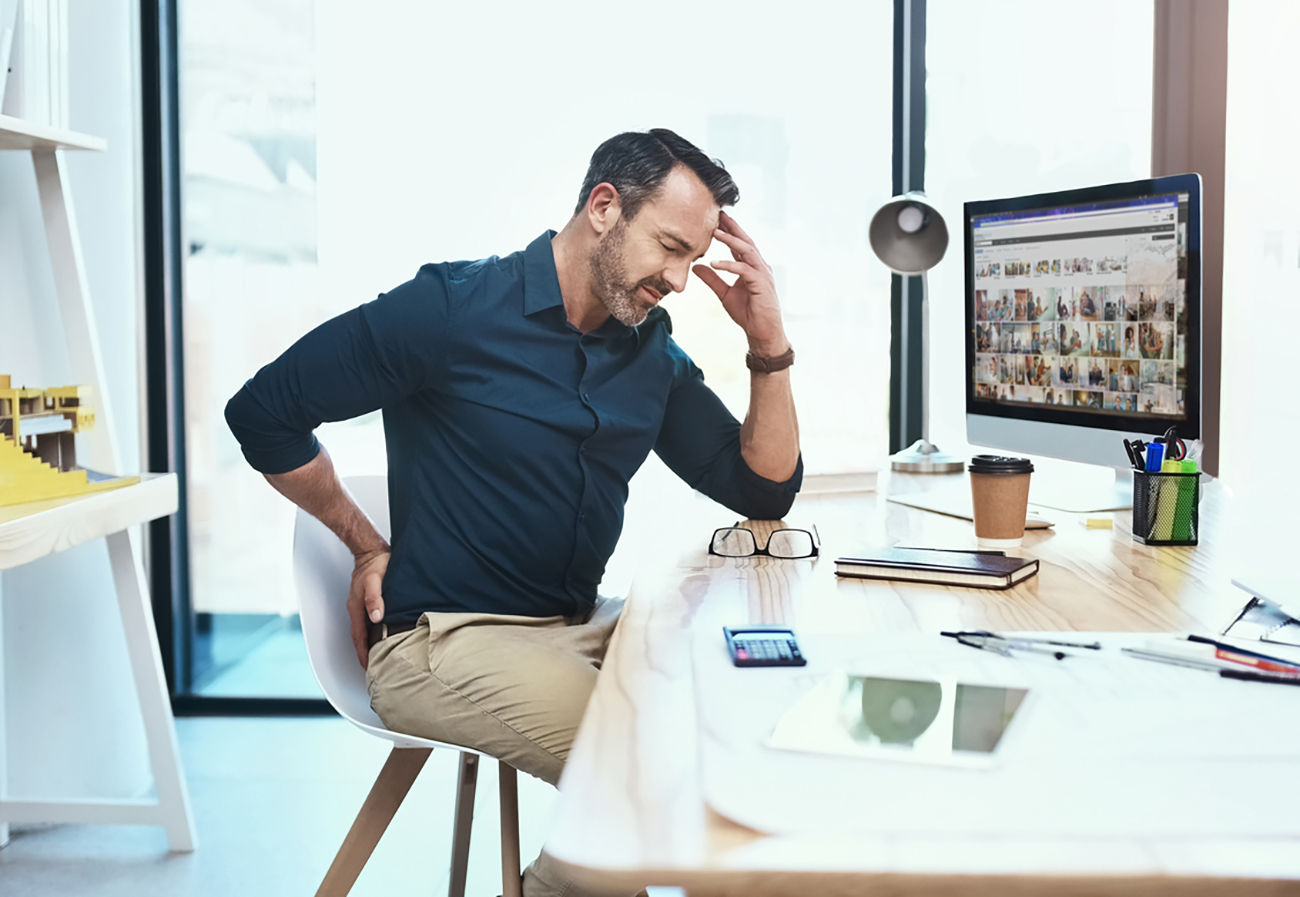 Shot of a mature businessman experiencing back pain while working at his desk