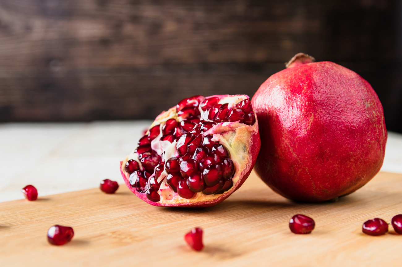 Whole fruit and halves of ripe pomegranate lie on a table on a wooden background. Juicy fresh pomegranates. Organic Bio fruits