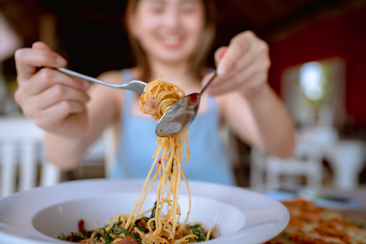 Young Asian woman rolling spaghetti while eating lunch in Italian cafe.