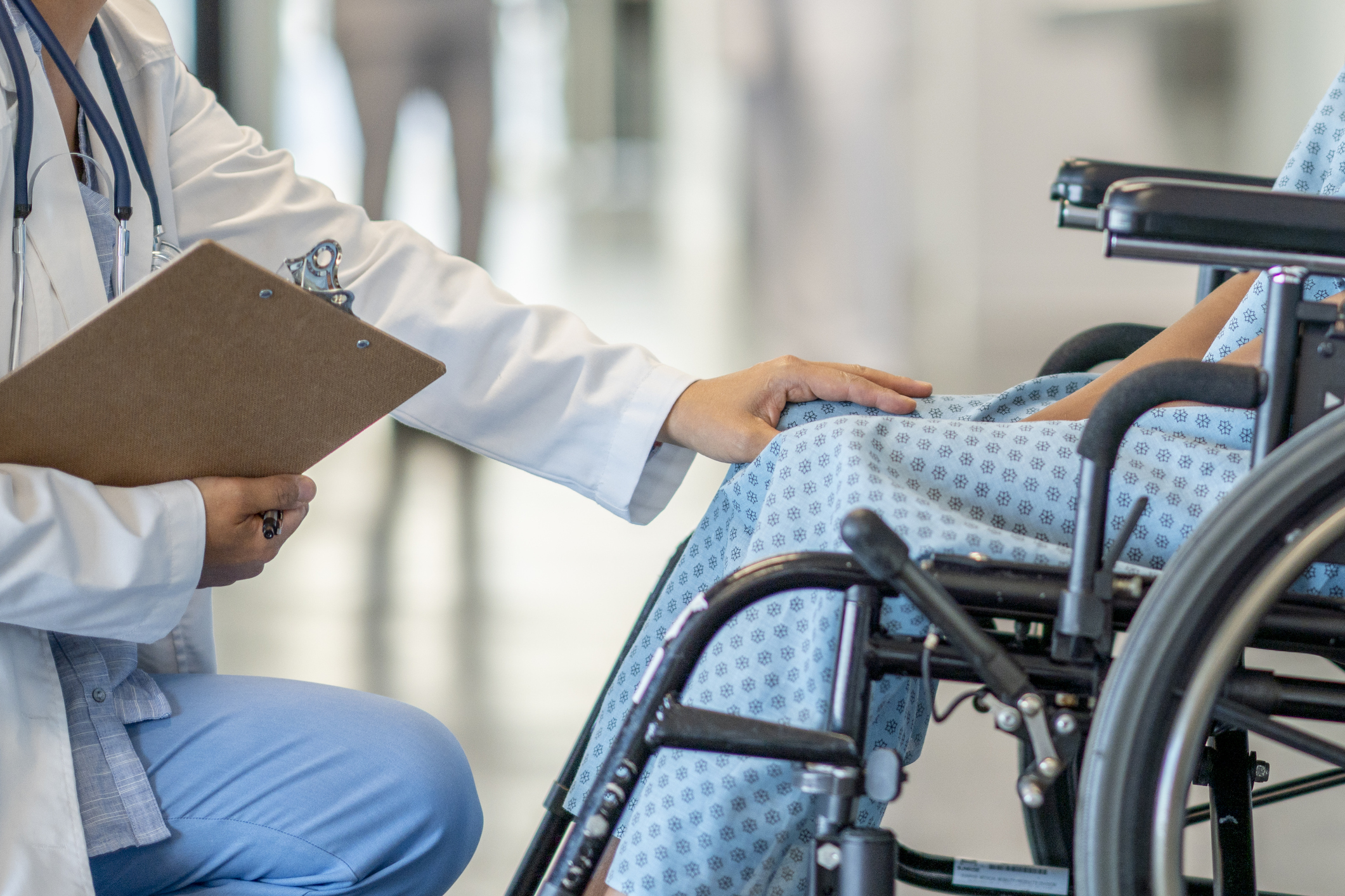 A teen girl with a disability sits in a wheelchair and is helped by a doctor who approaches her in an empathetic way.