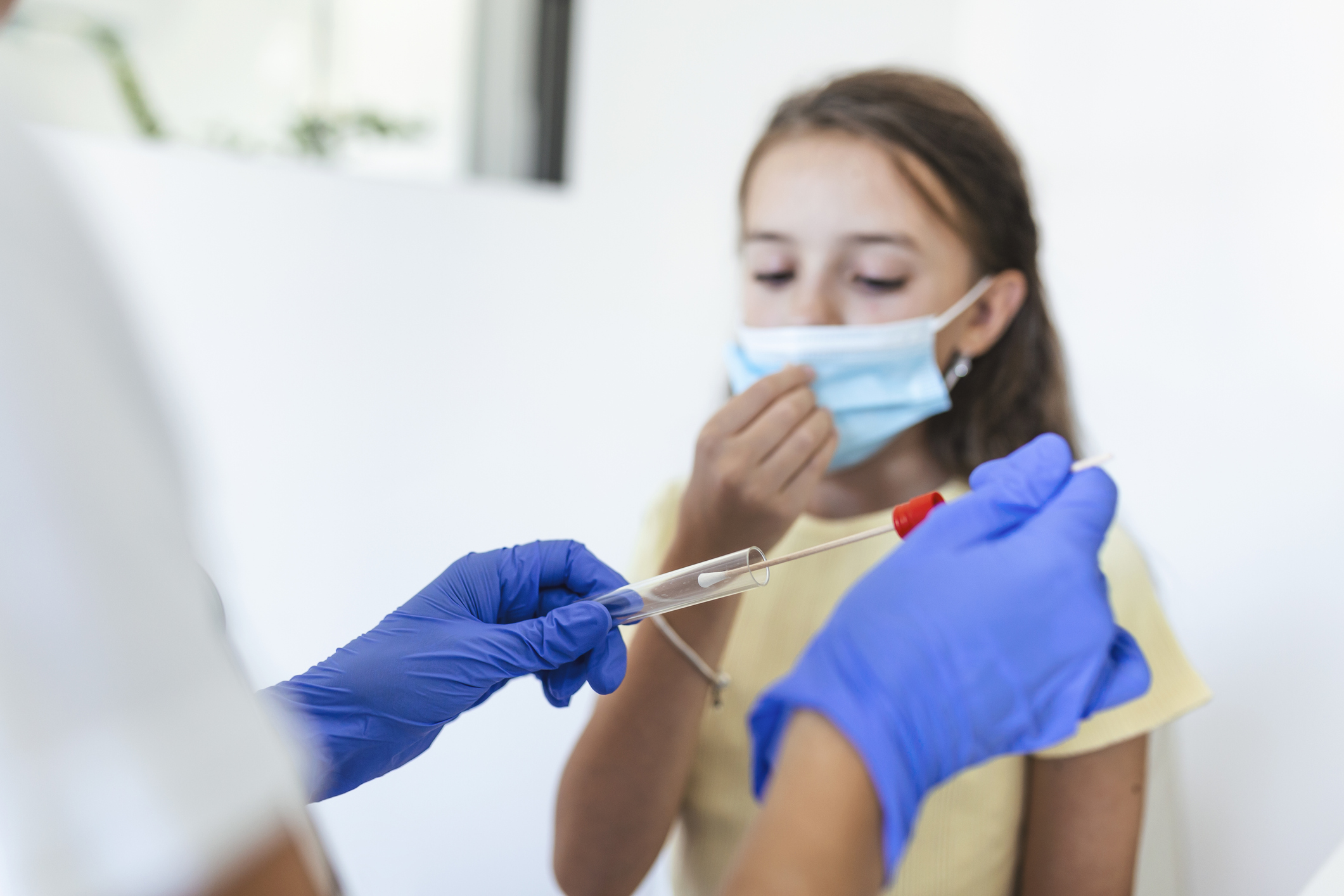 Nurse performing a mouth swab test on a little child. Girl going through PCR testing due to COVID-19 pandemic. Female doctor using cotton swab while PCR testing small girl
