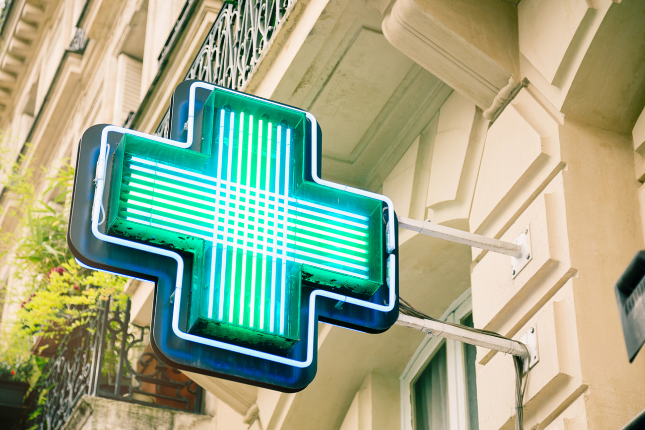 French pharmacy neon sign in front of Parisian apartments.