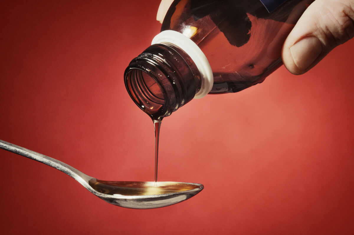 Thick syrup is being poured into a teaspoon. Male hands (myself) partially visibile. Slightly toned.