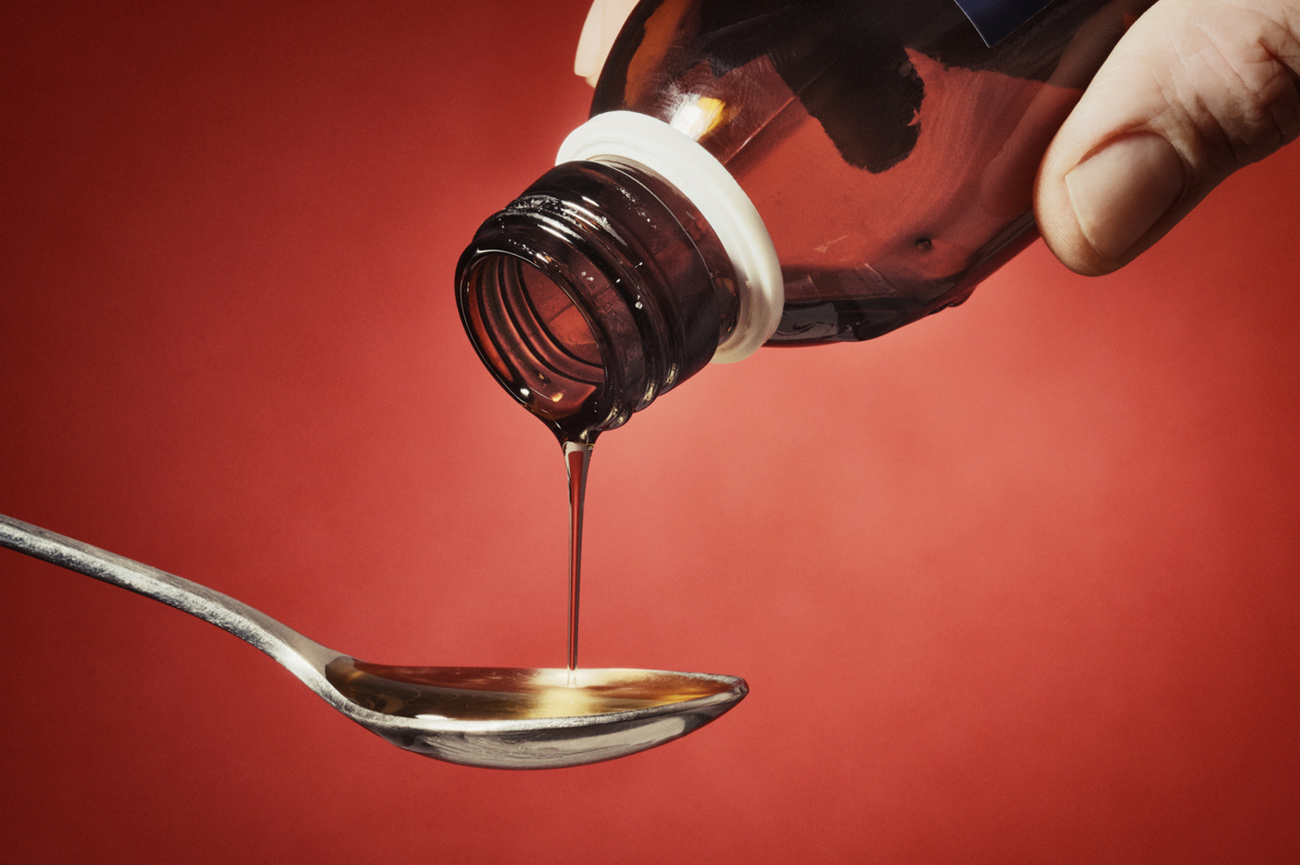 Thick syrup is being poured into a teaspoon. Male hands (myself) partially visibile. Slightly toned.