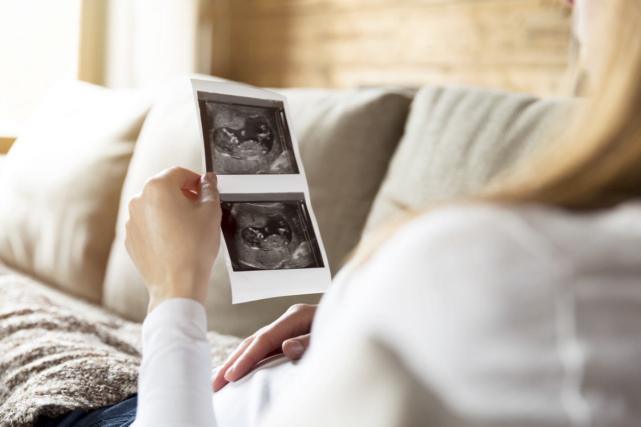Pregnant woman expecting newborn and holding ultrasound while lying comfortably on couch