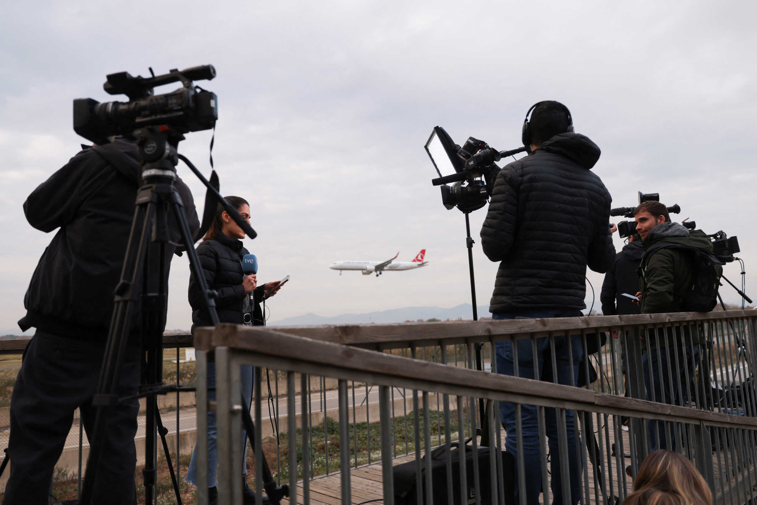 A plane flies in the background as journalists work, after a commercial airplane flying from Morocco to Turkey made an emergency landing in Barcelona's El Prat airport in the early hours and 28 would-be migrants on board ran away across the tarmac in Barcelona, Spain December 7, 2022. REUTERS