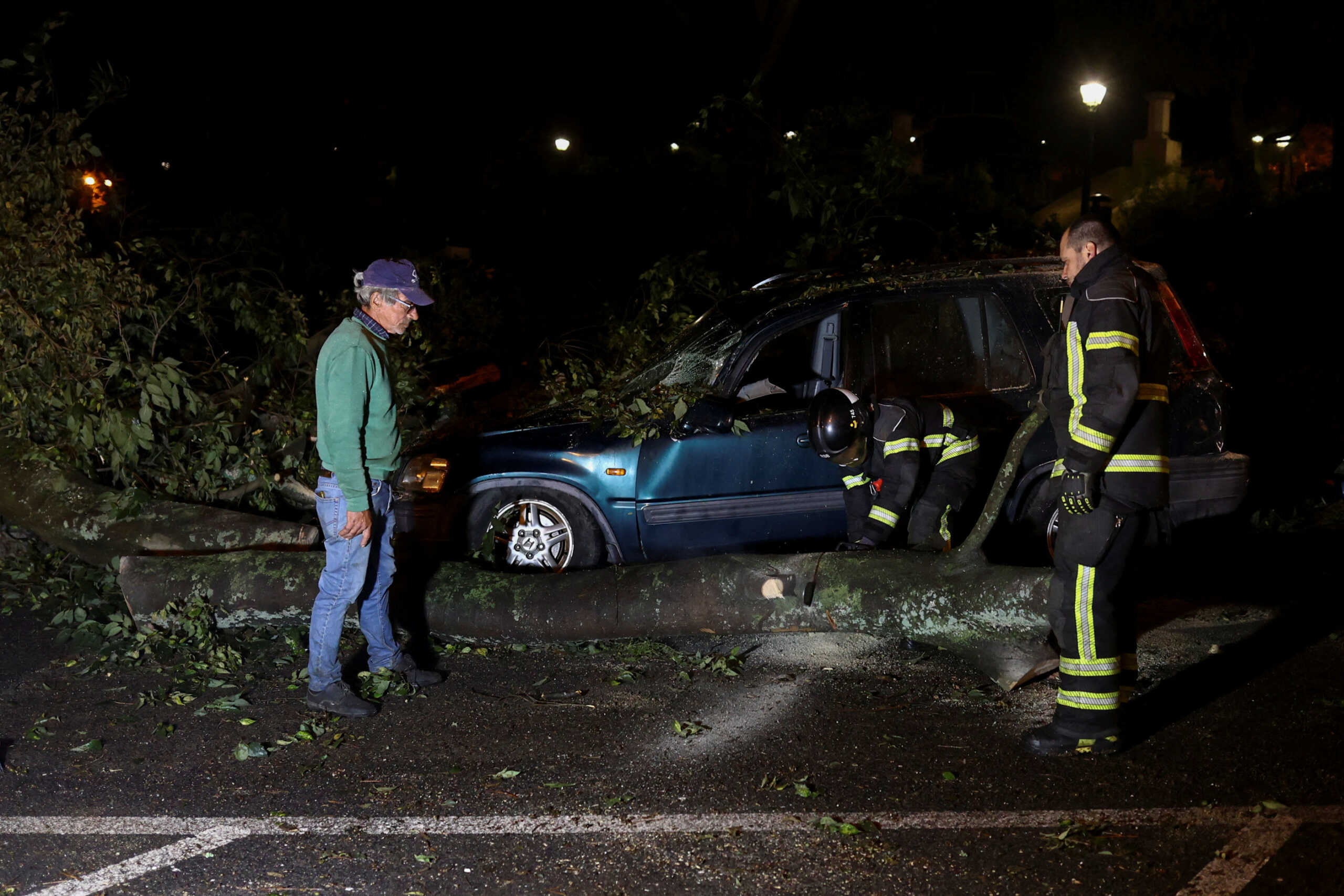 Firefighters cut a tree trunk that fell on a car after a tornado hit Lisbon, Portugal, November 8, 2022. REUTERS
