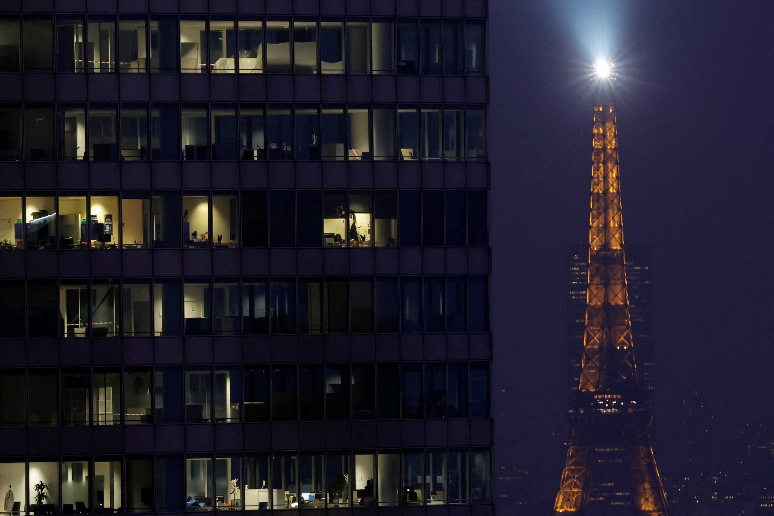 The Eiffel Tower lights the sky behind office lights illuminated at dusk in high rise buildings at La Defense business and financial district near Paris, France, December 5, 2022. REUTERS