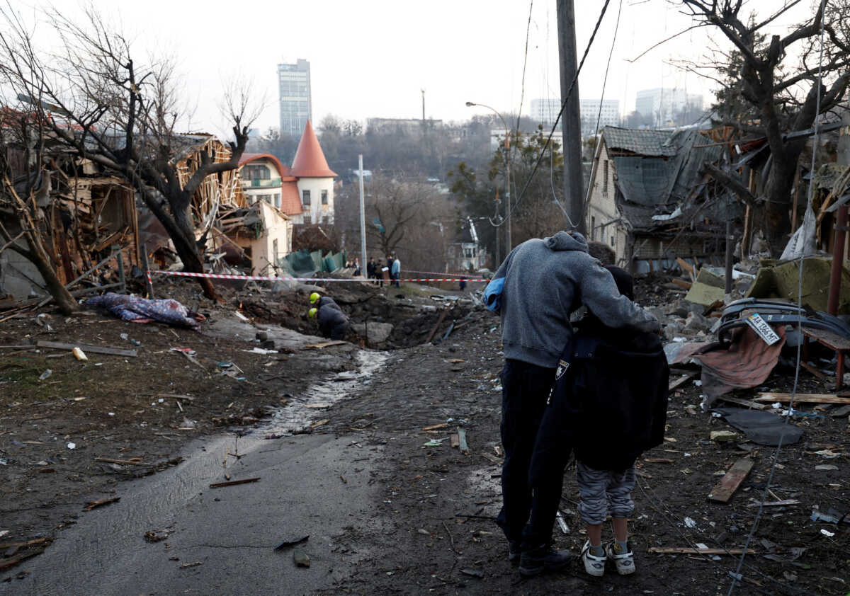 A local resident embraces his son as they stand next to a site of a Russian missile strike, amid Russia's attack on Ukraine, in Kyiv, Ukraine December 31, 2022. REUTERS