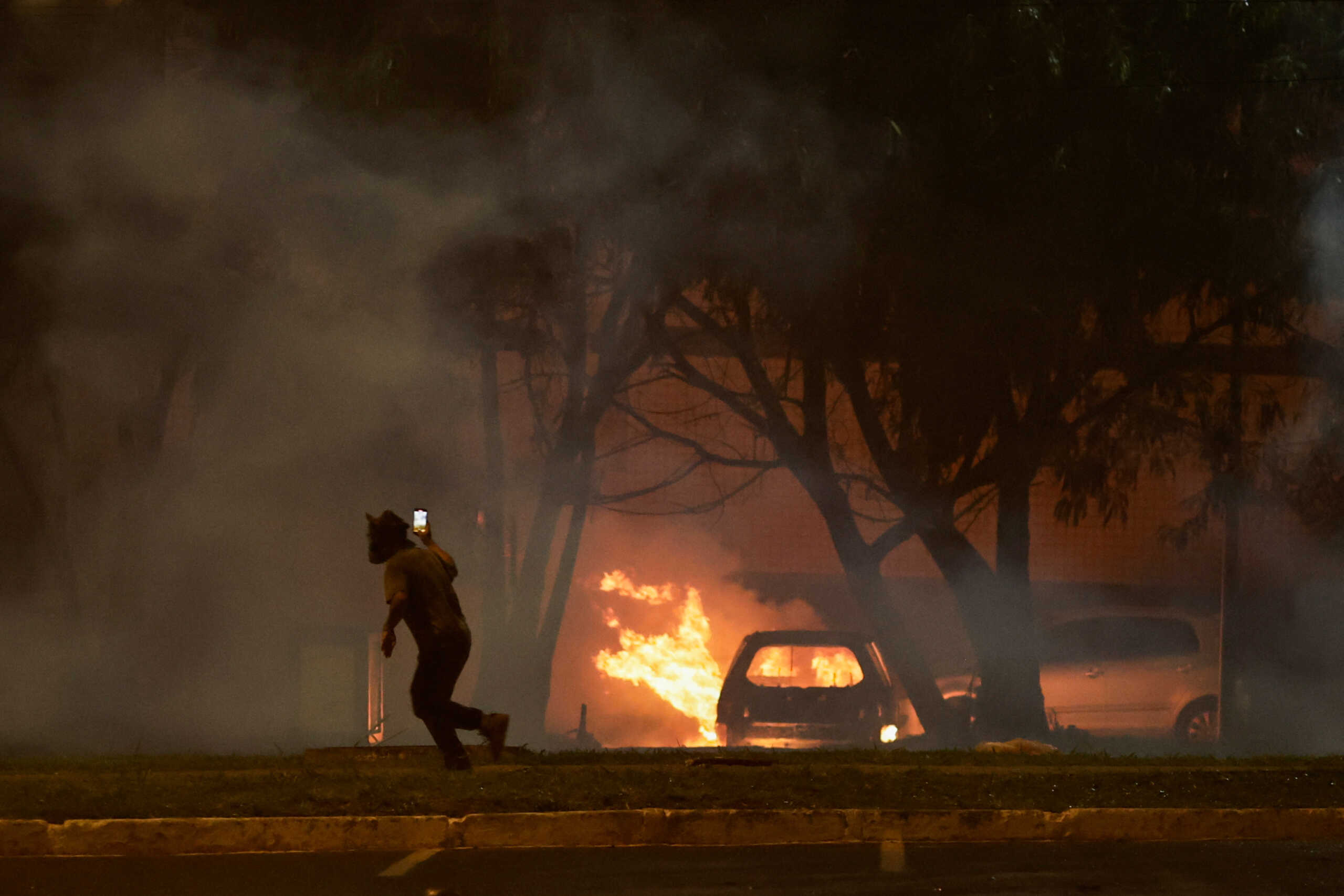 A man is seen near a car on fire as supporters of Brazil's President Jair Bolsonaro protest after supreme court justice Alexandre de Moraes ordered a temporary arrest warrant of indigenous leader Jose Acacio Serere Xavante for alleged anti-democratic acts, in Brasilia, Brazil, December 12, 2022. REUTERS