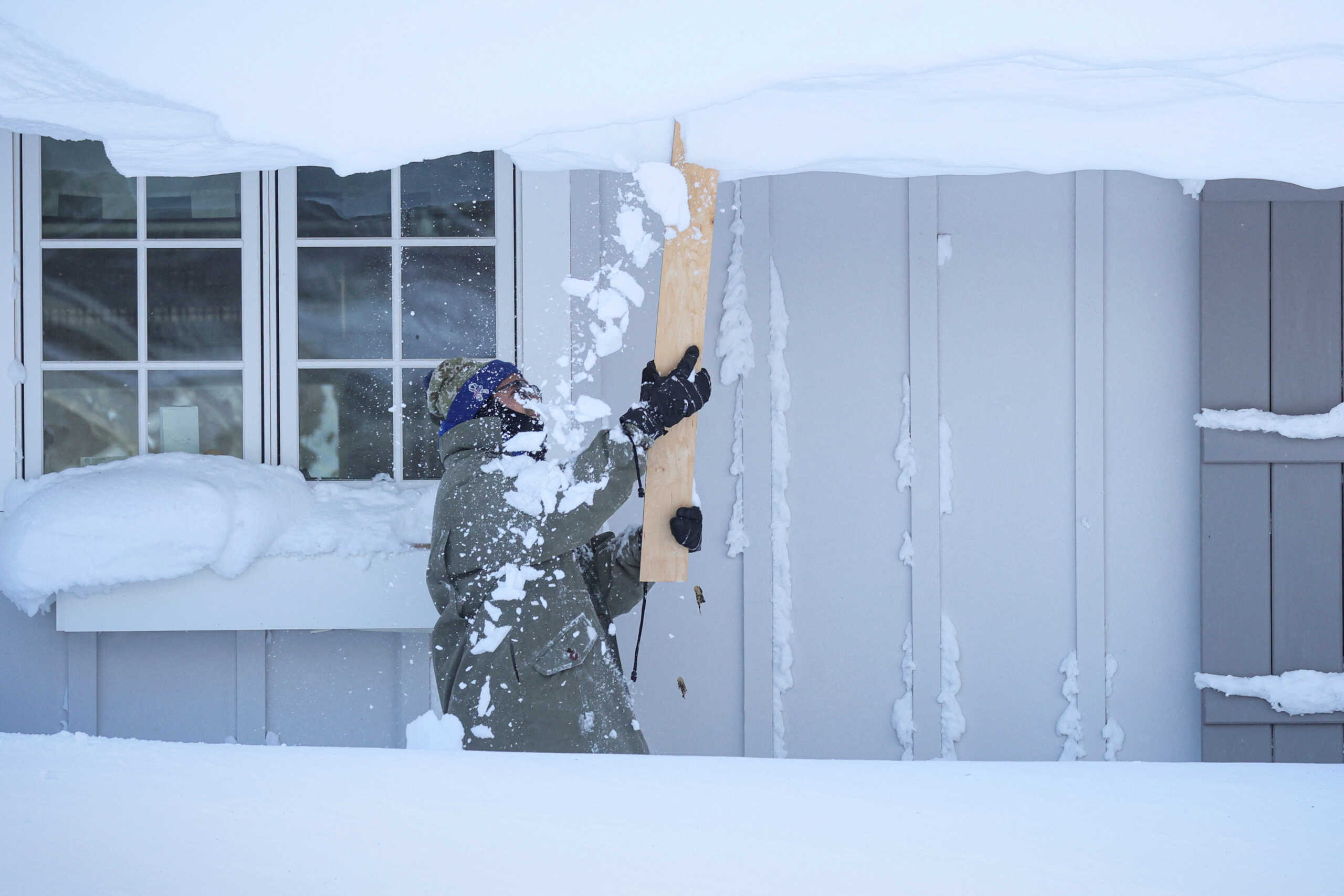 A man clears snow from his roof following a winter storm that hit the Buffalo region in Amherst, New York, U.S., December 25, 2022.  REUTERS