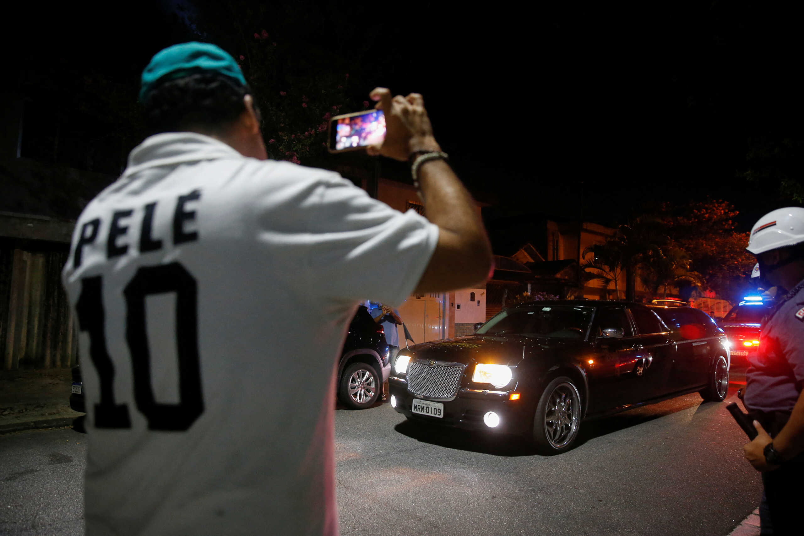 A fan wearing a shirt with Brazilian soccer legend Pele's name on it, records images as a vehicle transports Pele's body, in Santos, Brazil, January 2, 2023. REUTERS