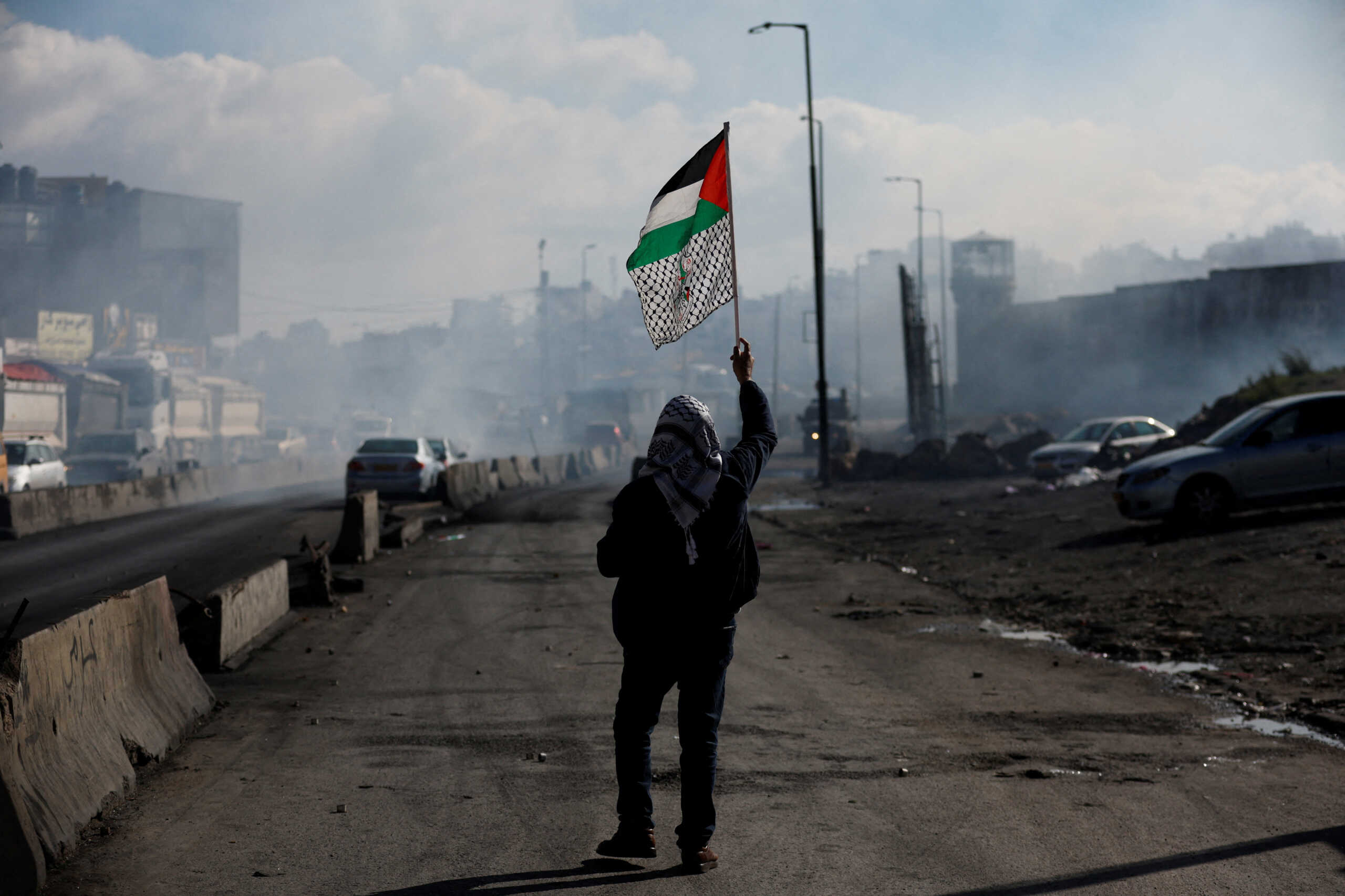 FILE PHOTO: A man walks with a Palestinian flag, as Palestinians clash with Israeli forces during a protest against what organizers say are Israel's measures of keeping bodies of dead prisoners, near Qalandia in the Israeli-occupied West Bank December 27, 2022. REUTERS