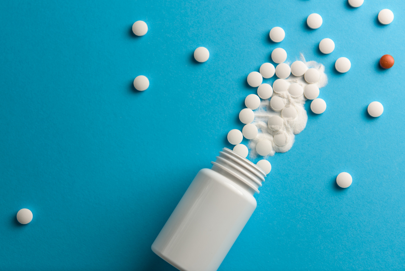 White pills spilled from a white bottle on a blue background