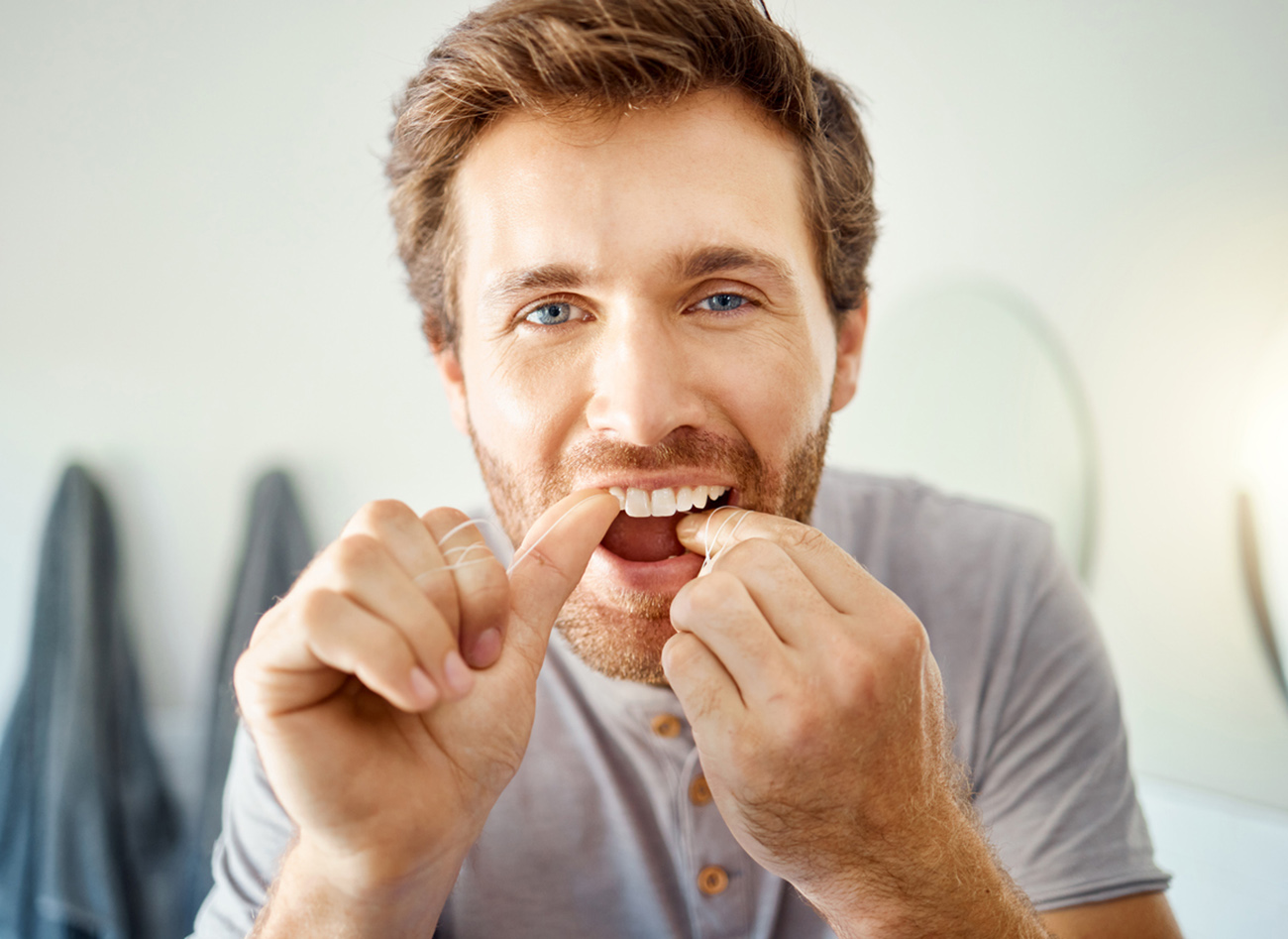 One handsome man flossing his teeth in a bathroom at home. Caucasian male using floss to prevent cavities while looking in a mirror in his apartment