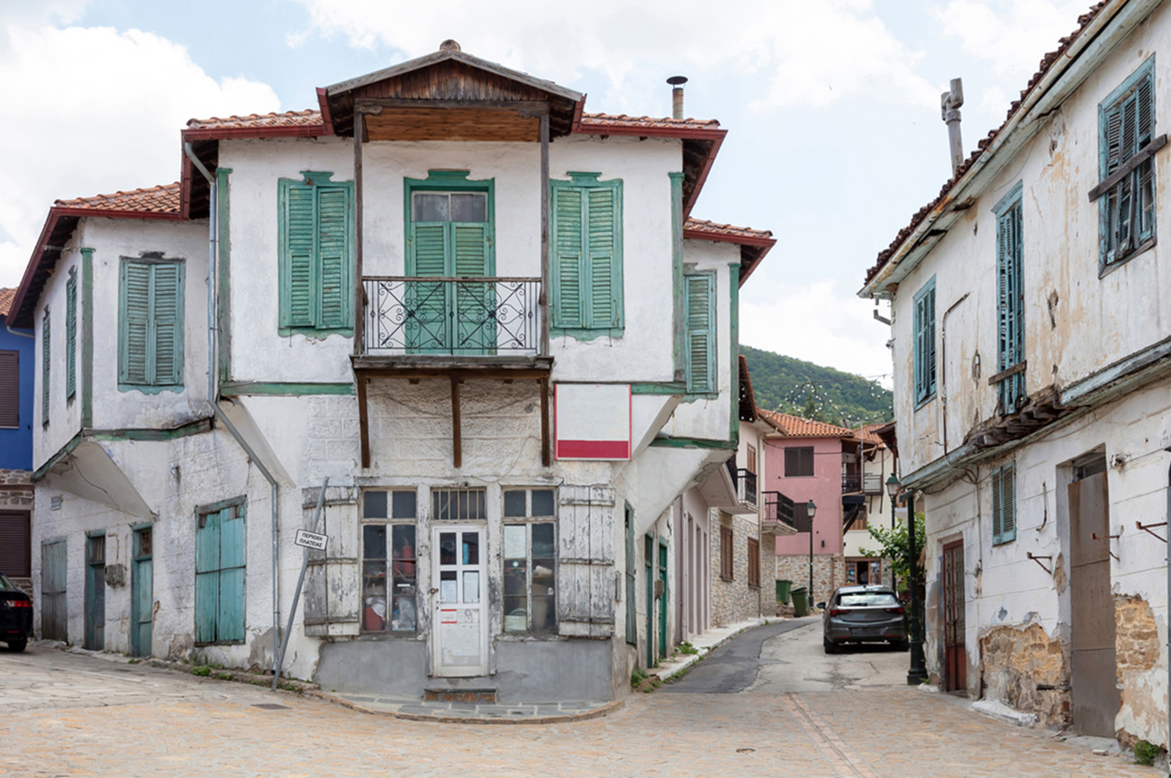 Greece, Arnaia village Chalkidiki. Facade of aged pealed two floor building, home and store, tile roof, covered balcony, Macedonian architecture, cobbled street