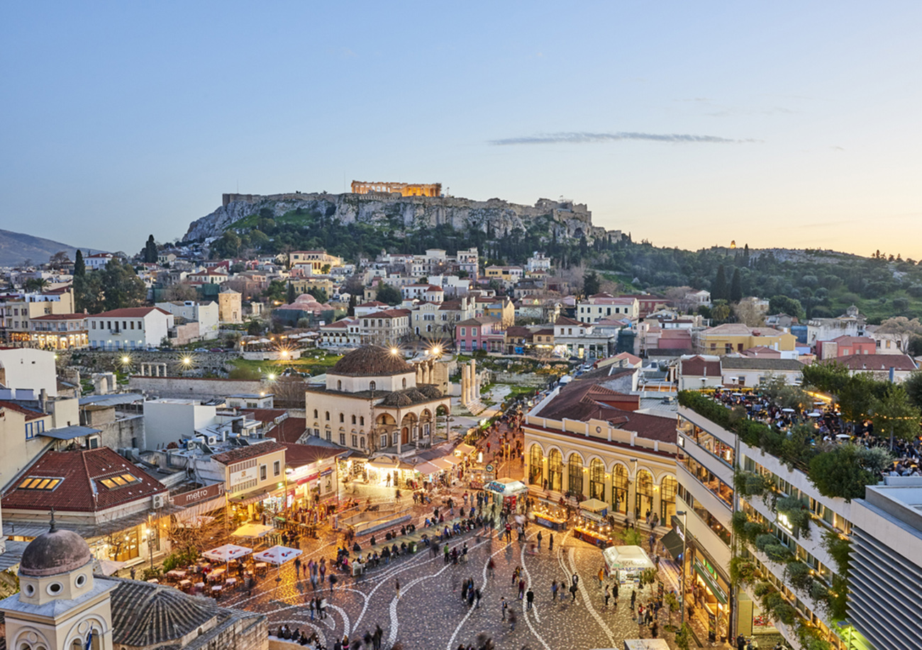 Athens, Greece - February 13, 2016: Aerial view of Athens at sunset with an illuminated Acropolis in the background. In foreground tourists and local people in Monastiraki Square. The clustered homes on the hill is known as Plaka.