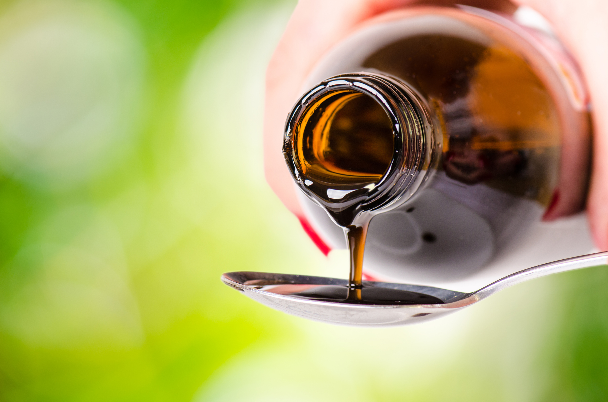 pouring a liquid on a spoon. Natural green background. Pharmacy and healthy background. Medicine. Cough and cold drug