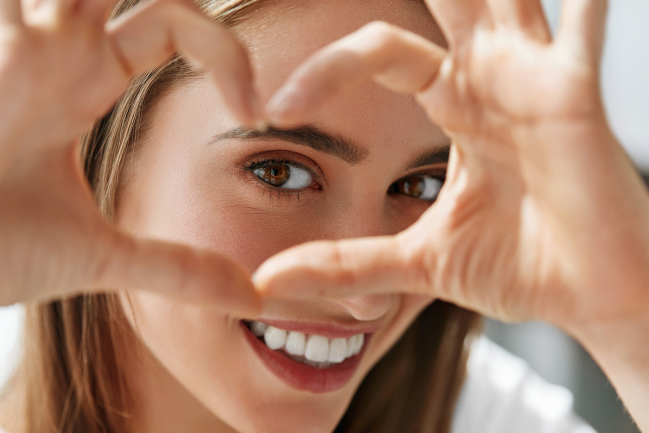 Healthy Eyes And Vision. Portrait Of Beautiful Happy Woman Holding Heart Shaped Hands Near Eyes. Closeup Of Smiling Girl With Healthy Skin Showing Love Sign. Eyecare. High Resolution Image