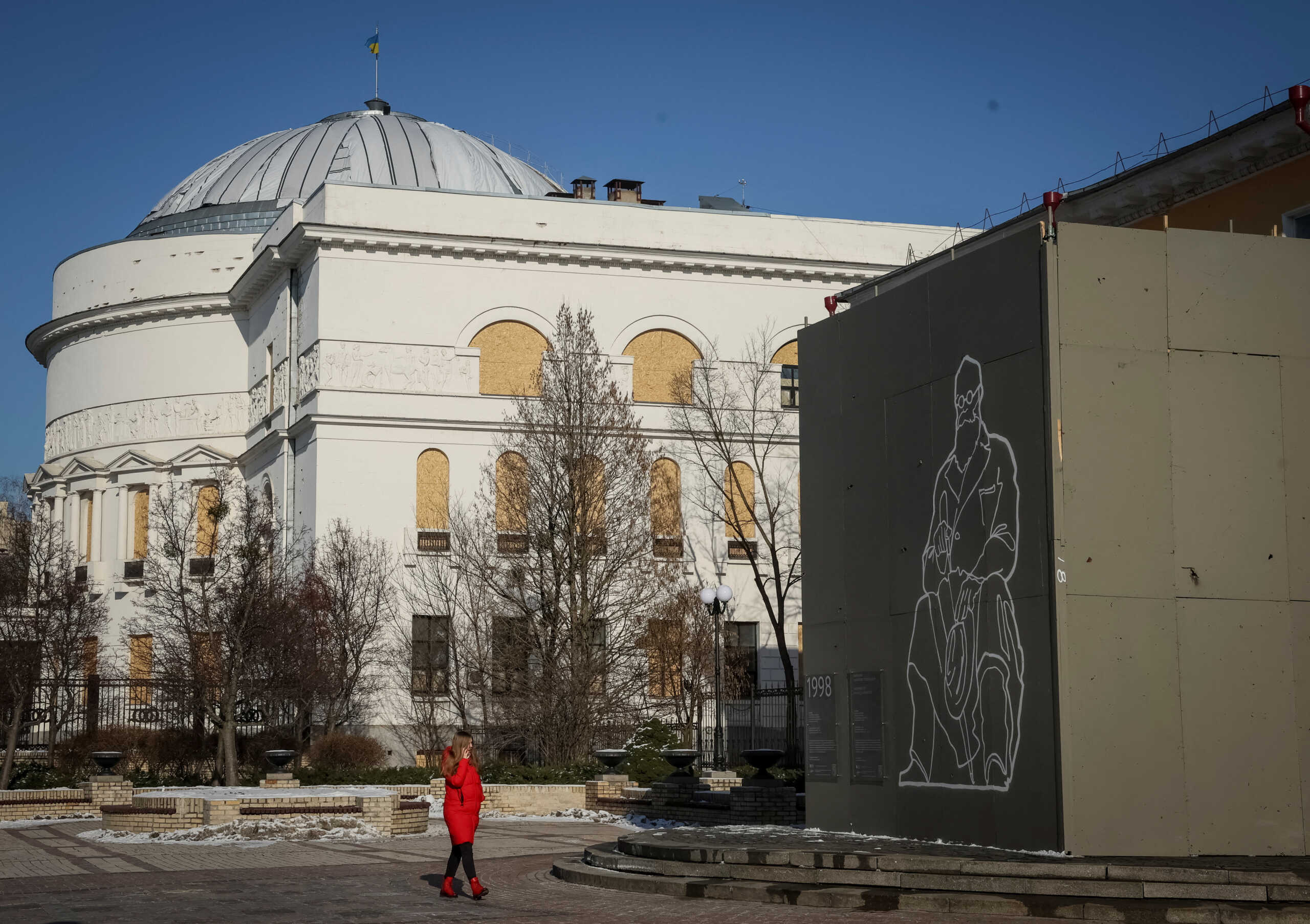 A woman walks near a monument of Ukraine's first president Mikhaylo Hrushevsky and a historical building covered with a protective construction to protect against shelling, amid Russia's invasion, in central Kyiv, Ukraine February 8, 2023. REUTERS
