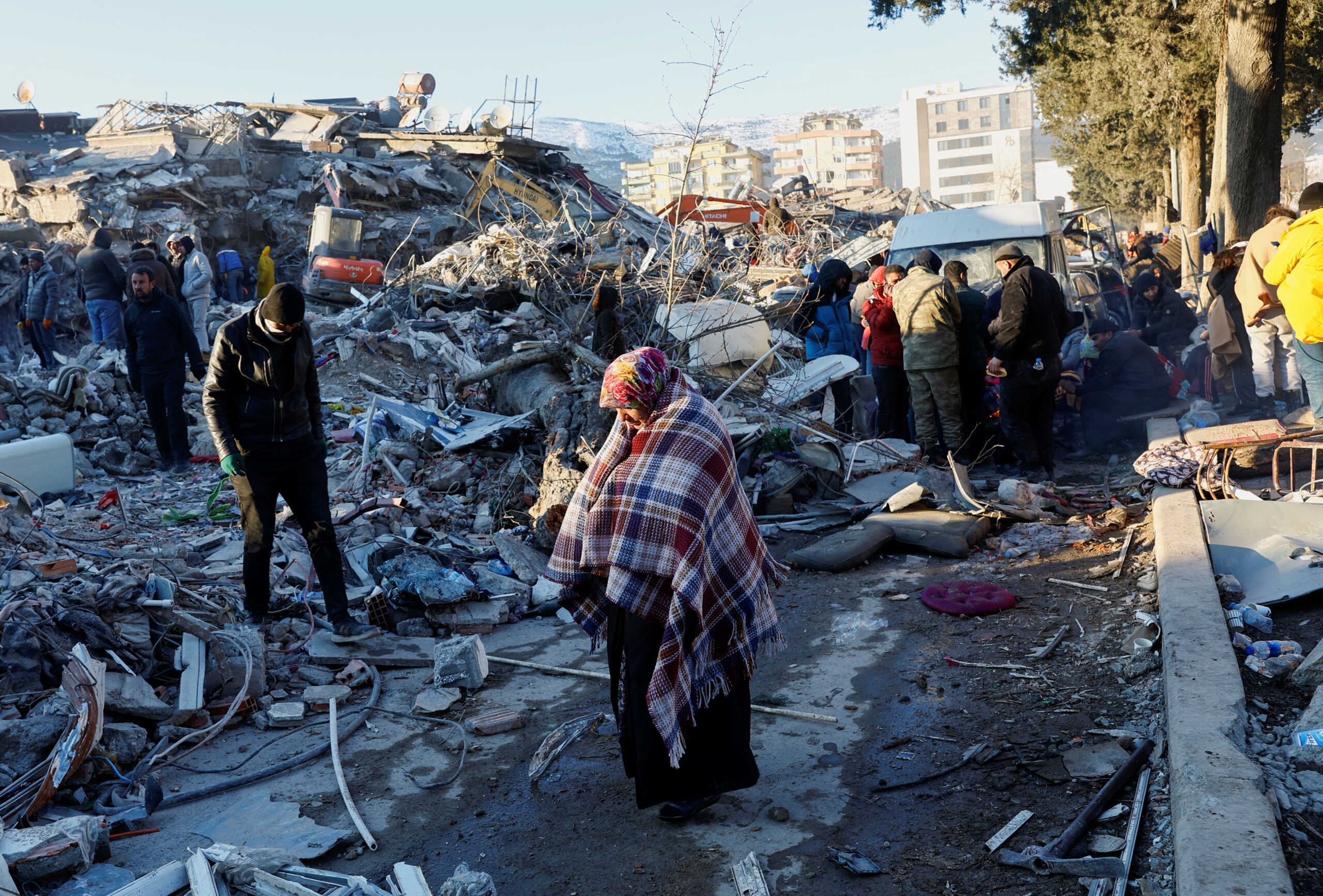 A woman stands near rubble and damages near the site of a collapsed buidling in the aftermath of an earthquake, in Kahramanmaras, Turkey, February 8, 2023. REUTERS