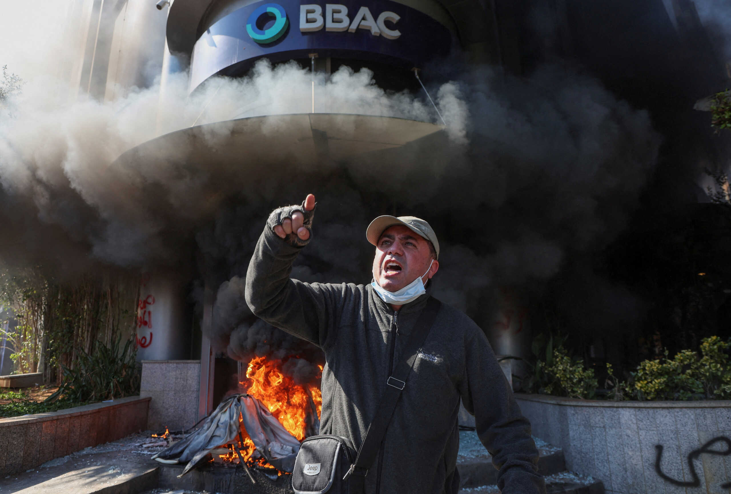 A demonstrator gestures near a bank, set on fire, during a protest organized by Depositors' Outcry, a group campaigning for angry depositors, against informal restrictions on cash withdrawals and deteriorating economic conditions in Beirut, Lebanon February 16, 2023. REUTERS