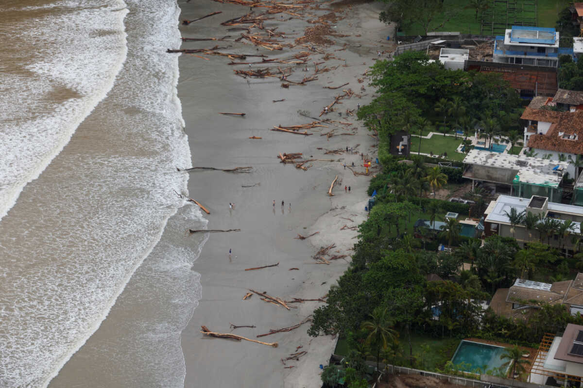 People walk on a beach near trees after severe rainfall in Sao Sebastiao, Brazil, February 20, 2023. REUTERS